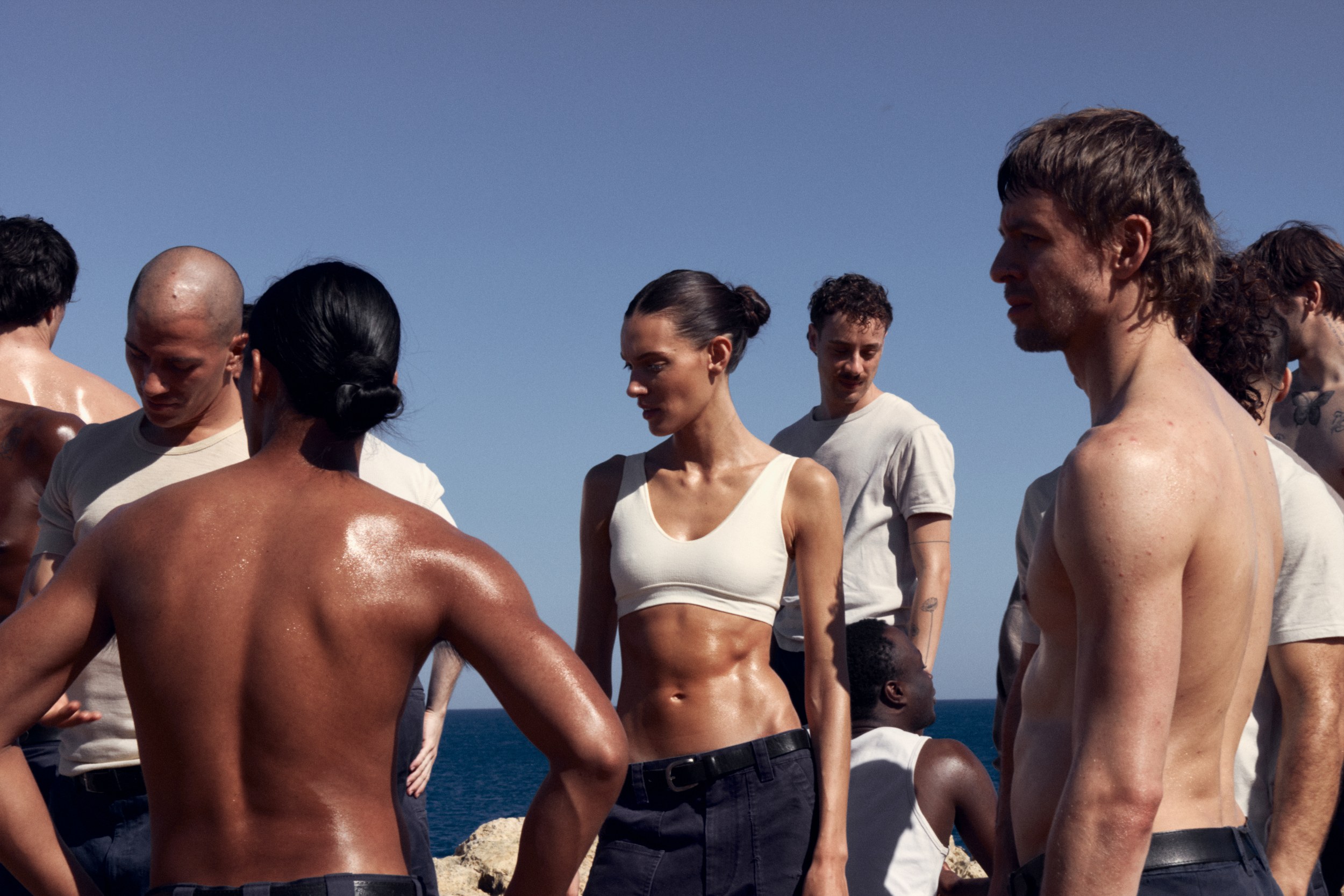 Group of fit individuals under the sun by the sea, showcasing athletic physiques.