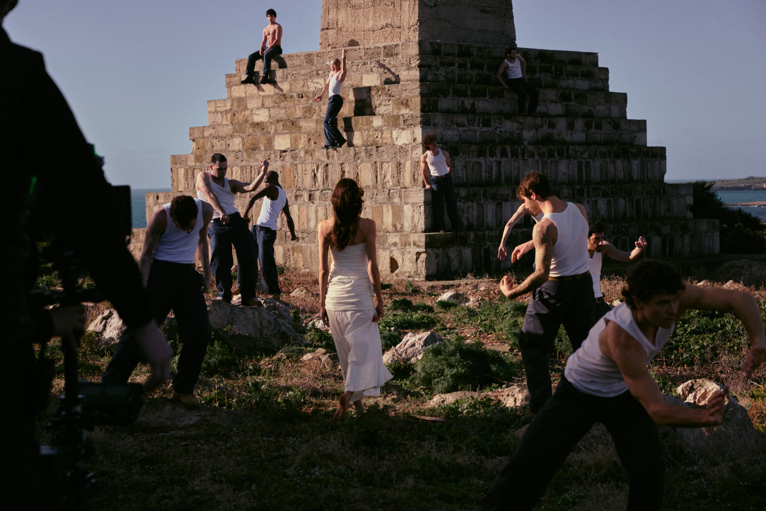 Group dances around a stone structure in outdoor setting.