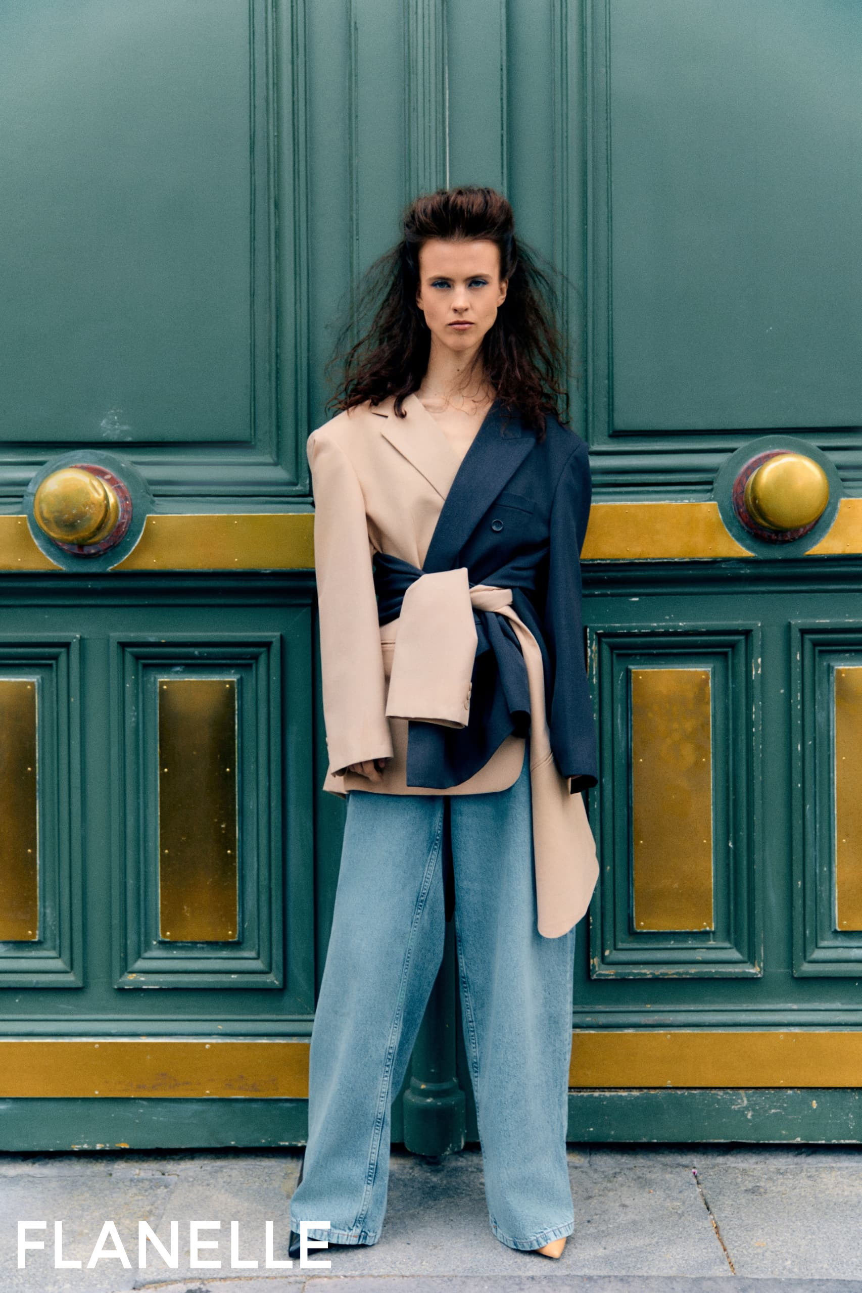 Fashion-forward outfit with two-tone blazer and wide-leg jeans against ornate door.