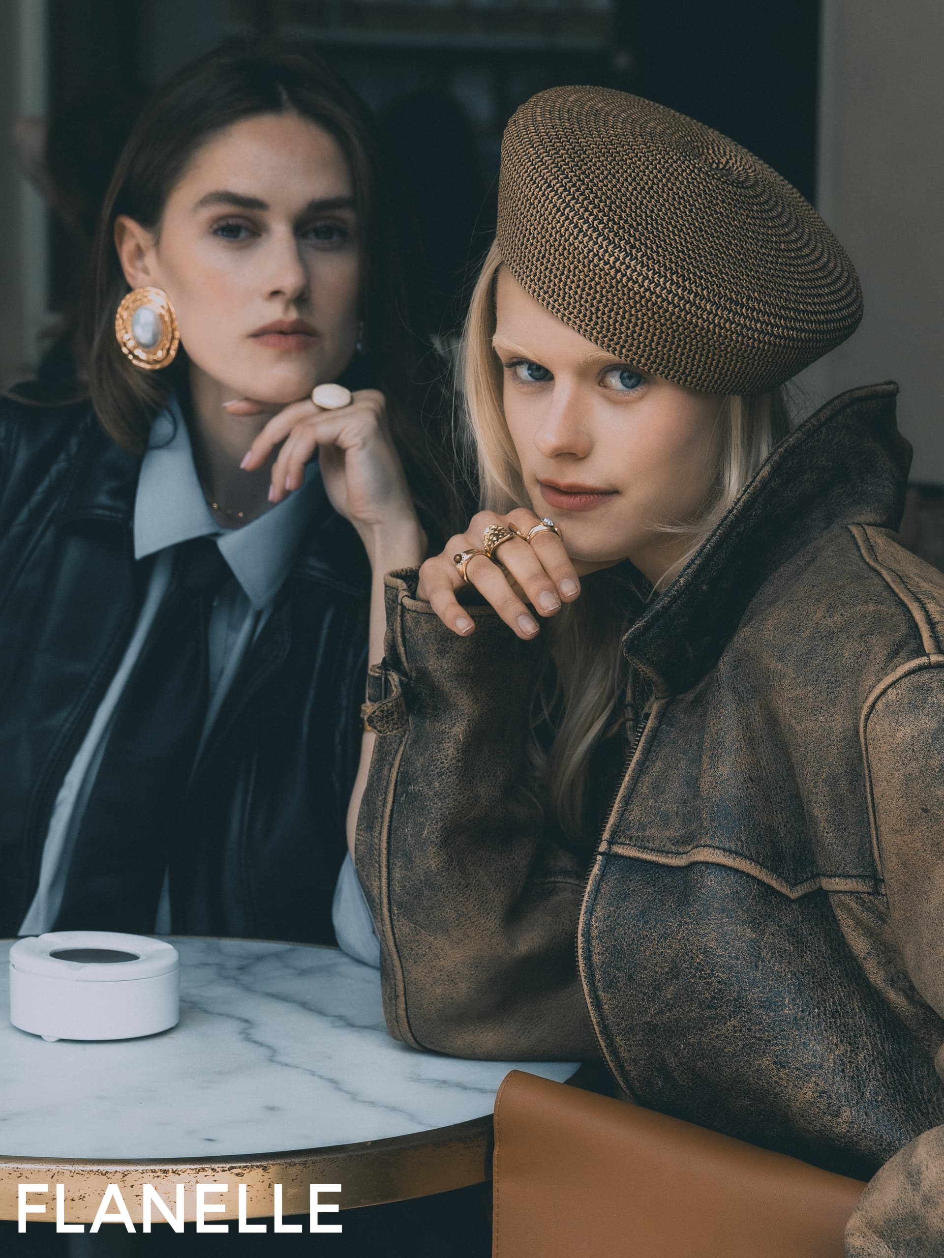 Two stylish women in chic outfits at a cafe table, showcasing fashion elegance.