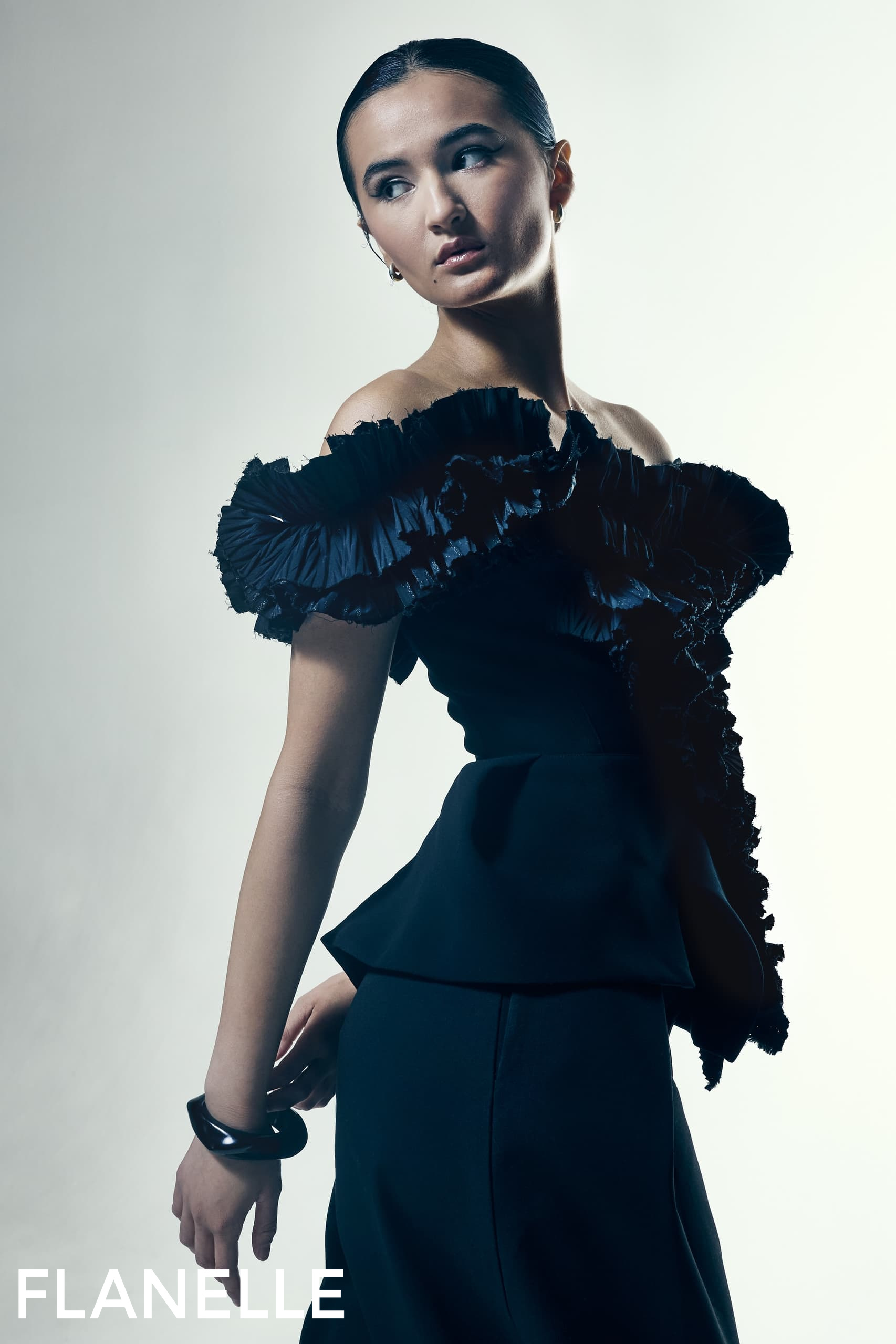 Fashion model in elegant, off-shoulder black dress by Flanelle magazine.