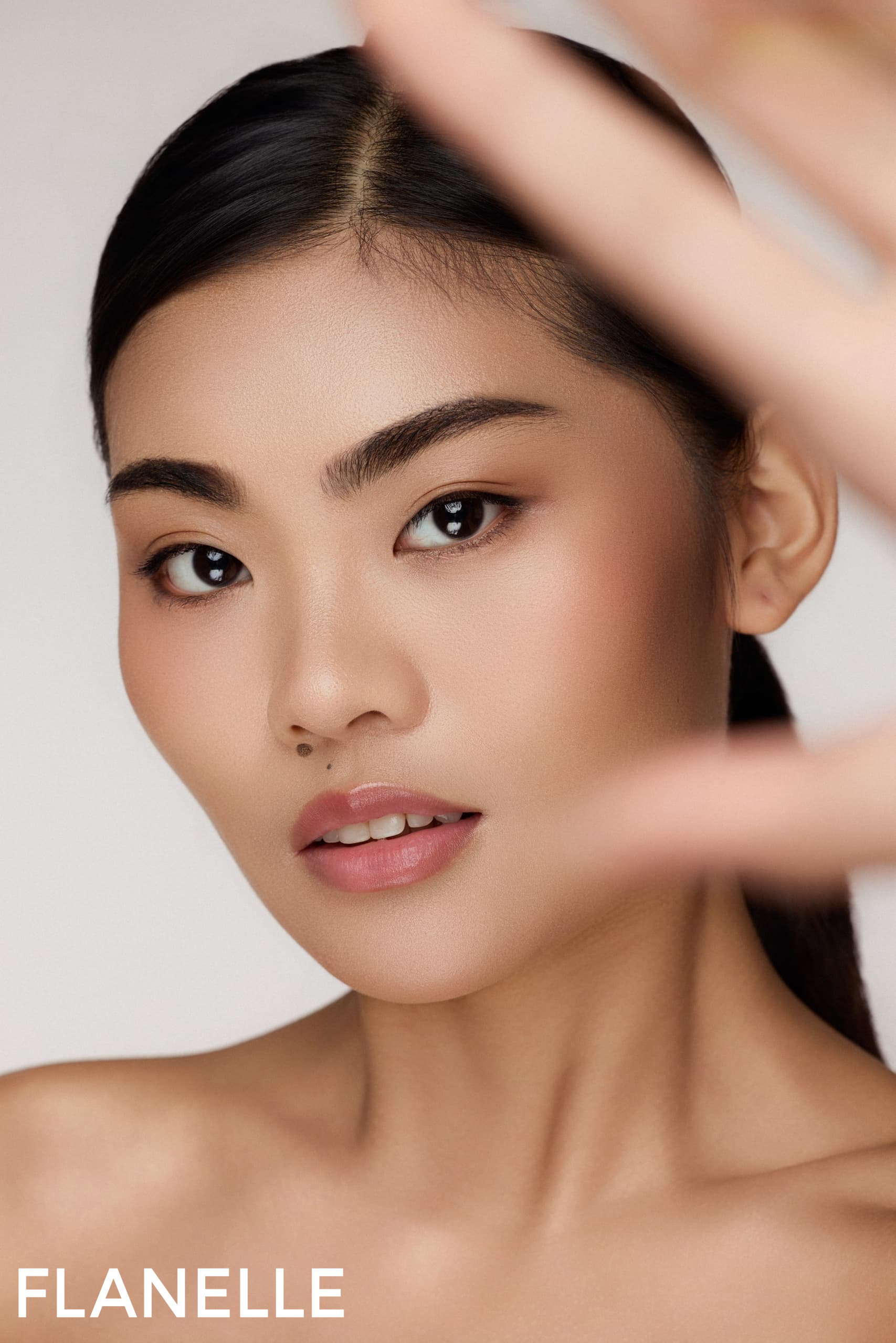 Elegant woman with flawless makeup and smooth skin, hand in foreground.