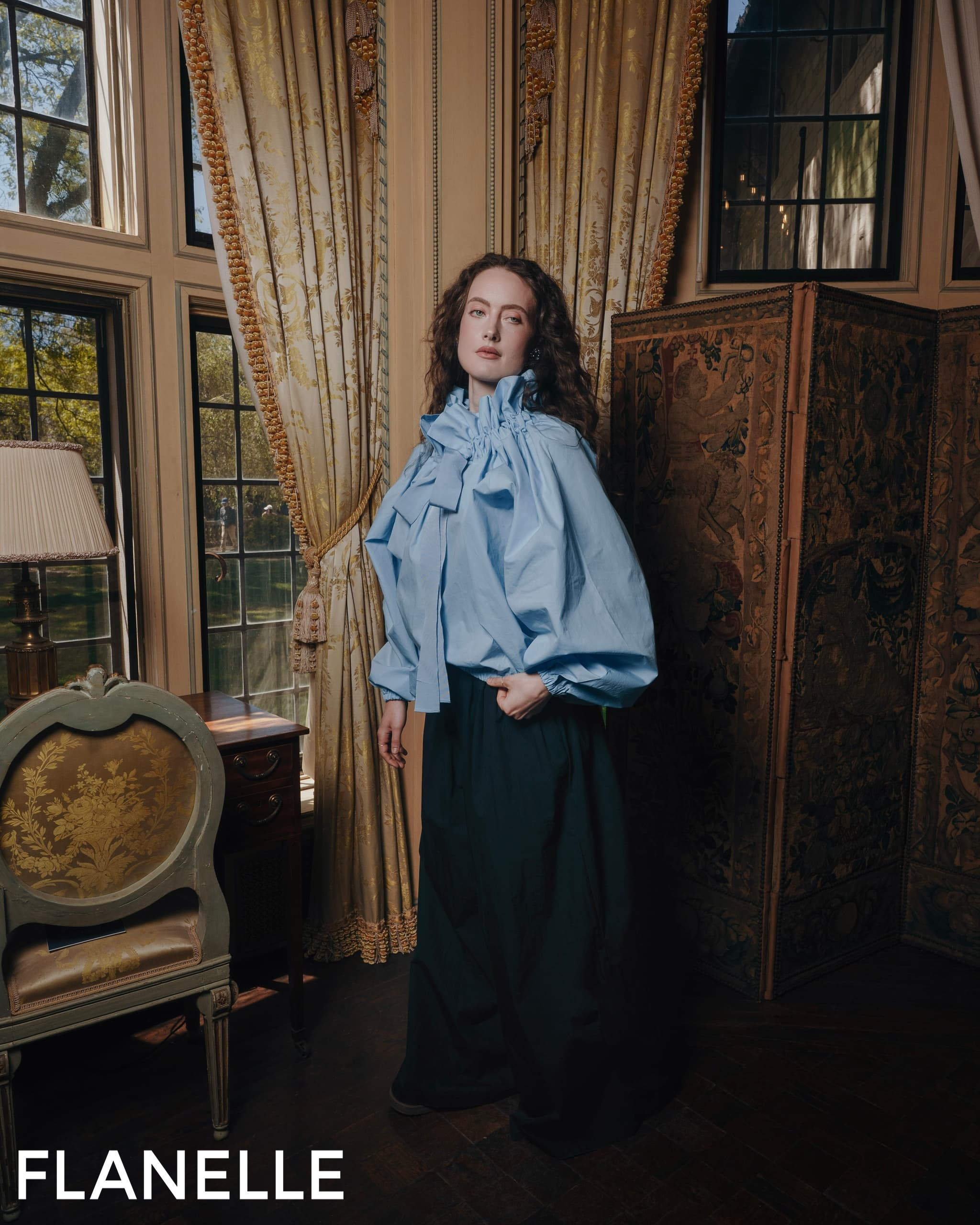 Fashionable woman in elegant attire by a window with vintage decor.