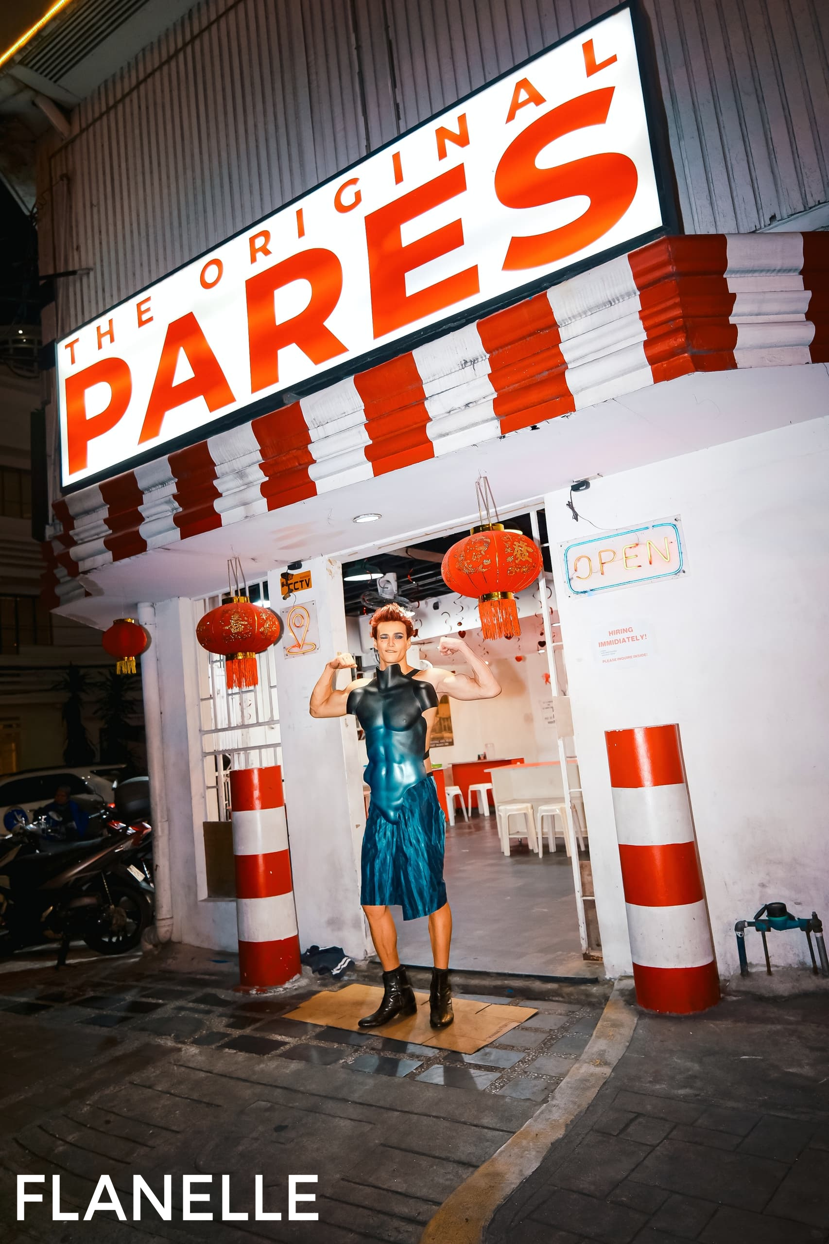 Person flexing outside The Original Pares restaurant at night.