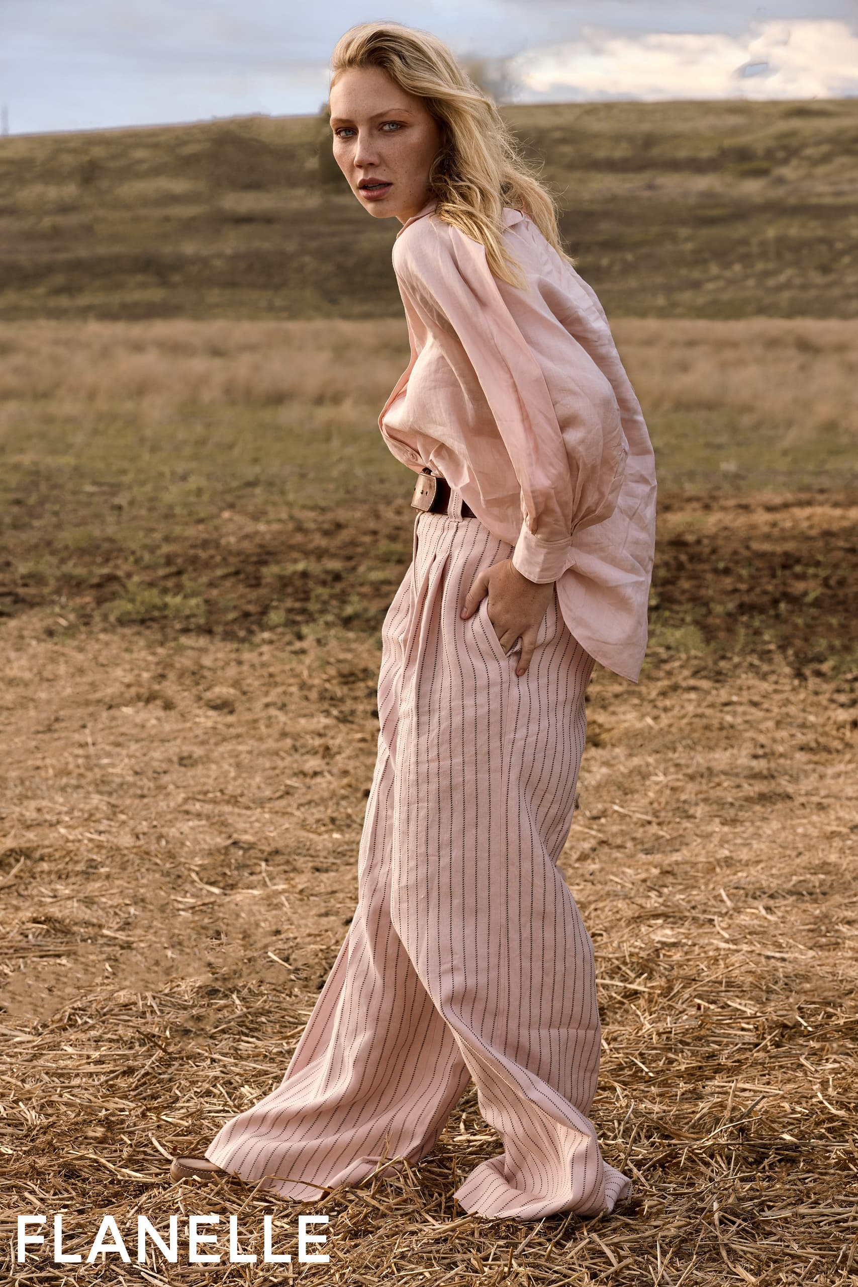 Woman in pink outfit standing in field, rustic background. Fashionable autumn look.