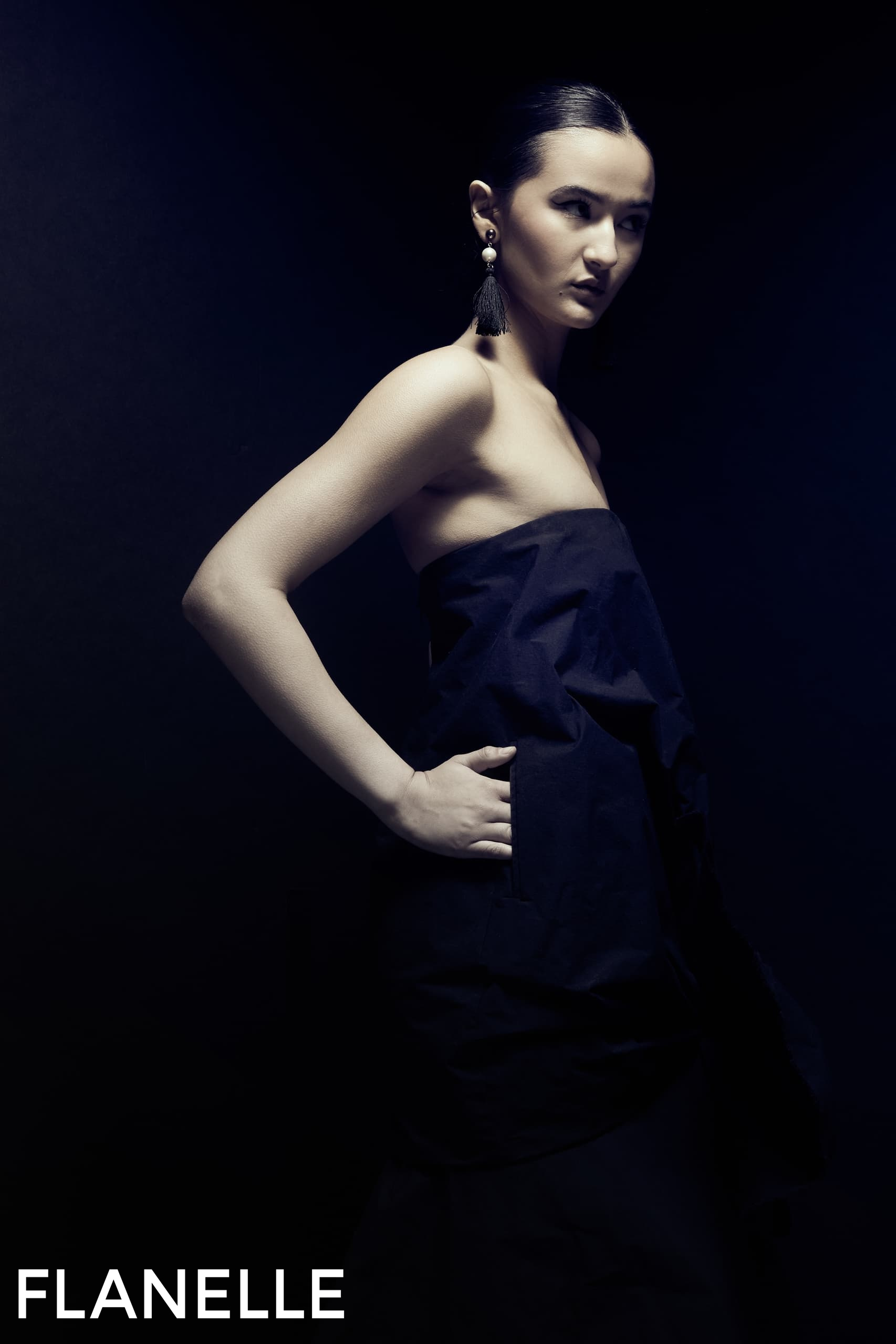 Elegant model in dramatic lighting wearing a sleek dress and tassel earrings.