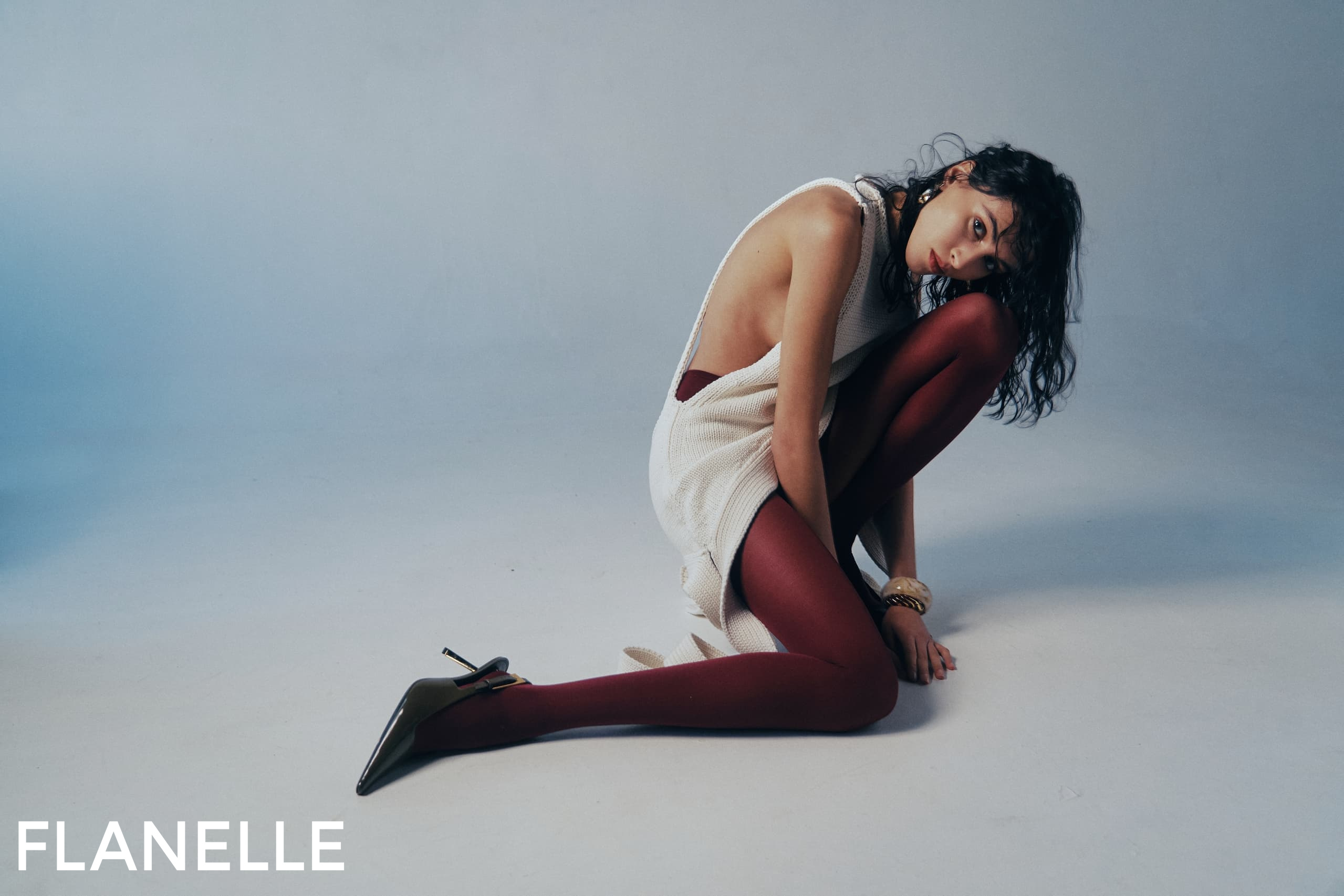 Model in stylish outfit with red tights and heels sitting on a studio floor.