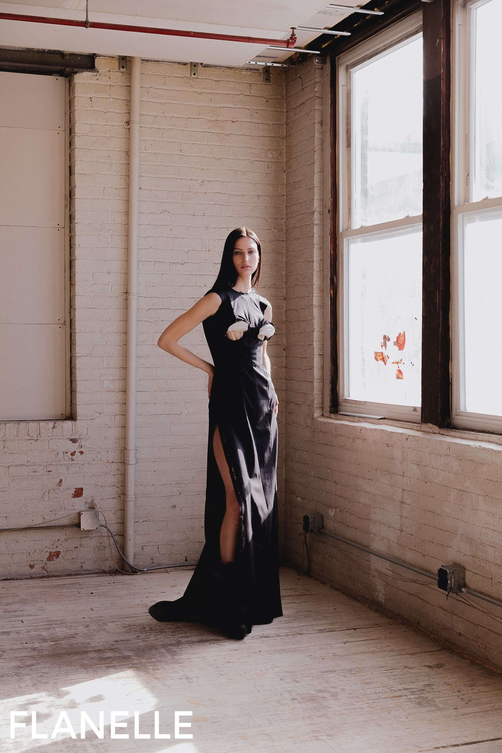 Fashionable woman in elegant black dress poses by sunlit window.