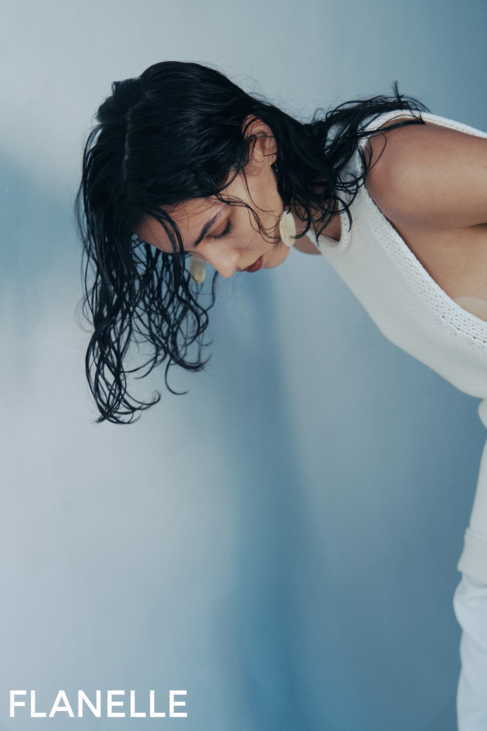 Wet-haired model in white, bending gracefully against a blue backdrop.