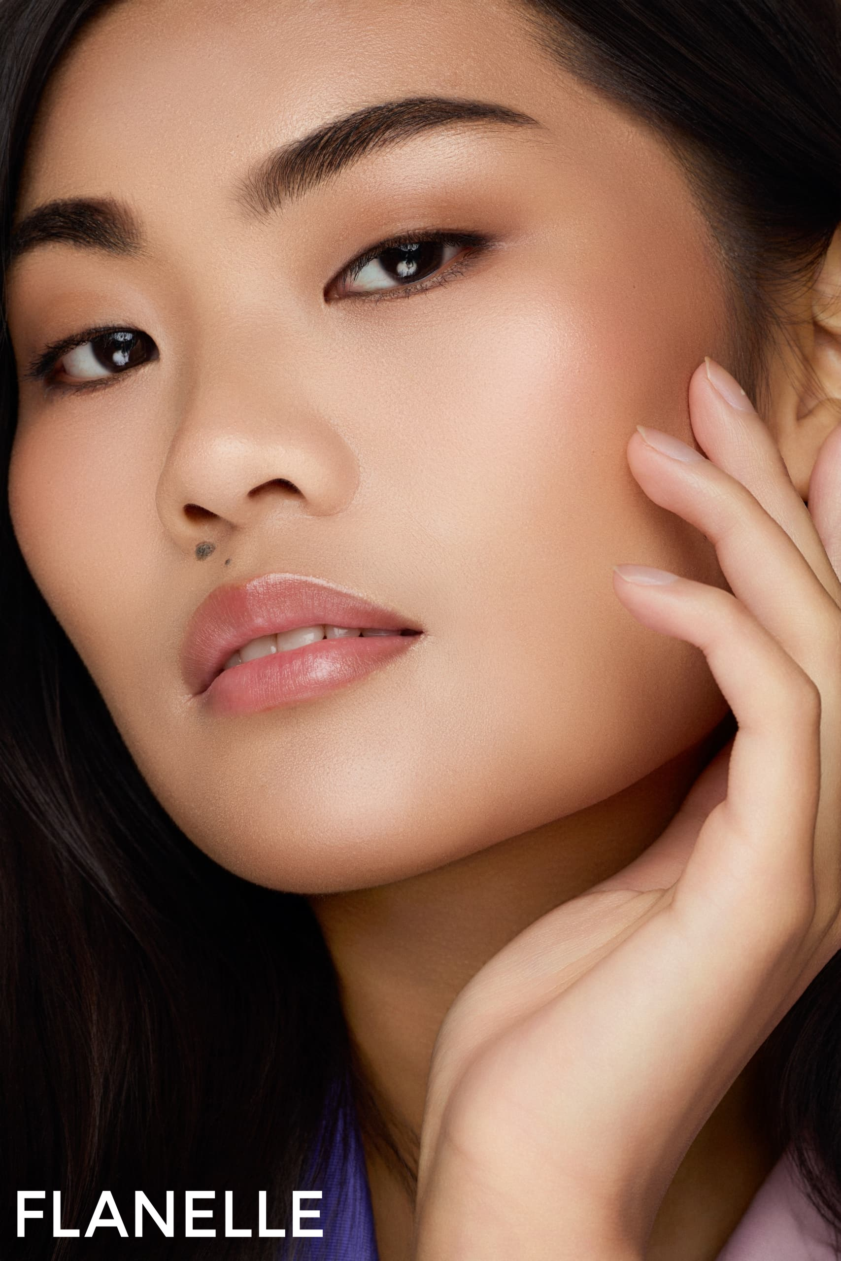 Close-up of a woman touching her face with a soft, natural makeup look.