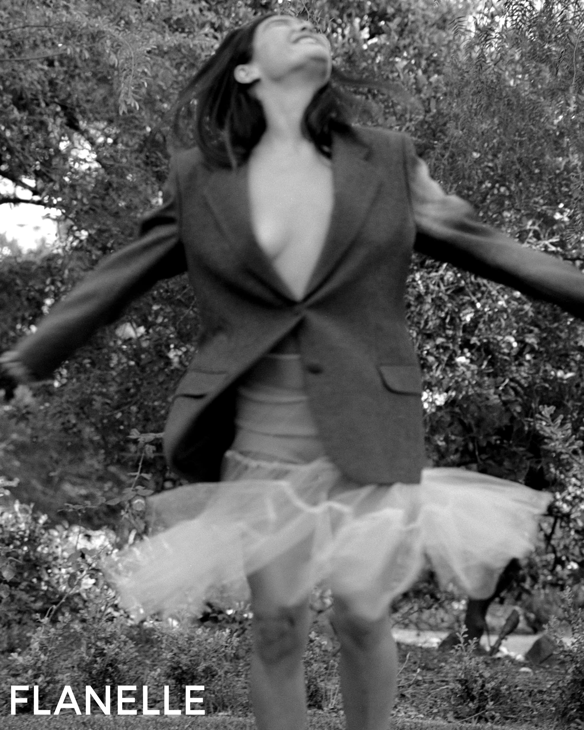 Woman in oversize blazer twirls in nature, wearing a tulle skirt, black and white.