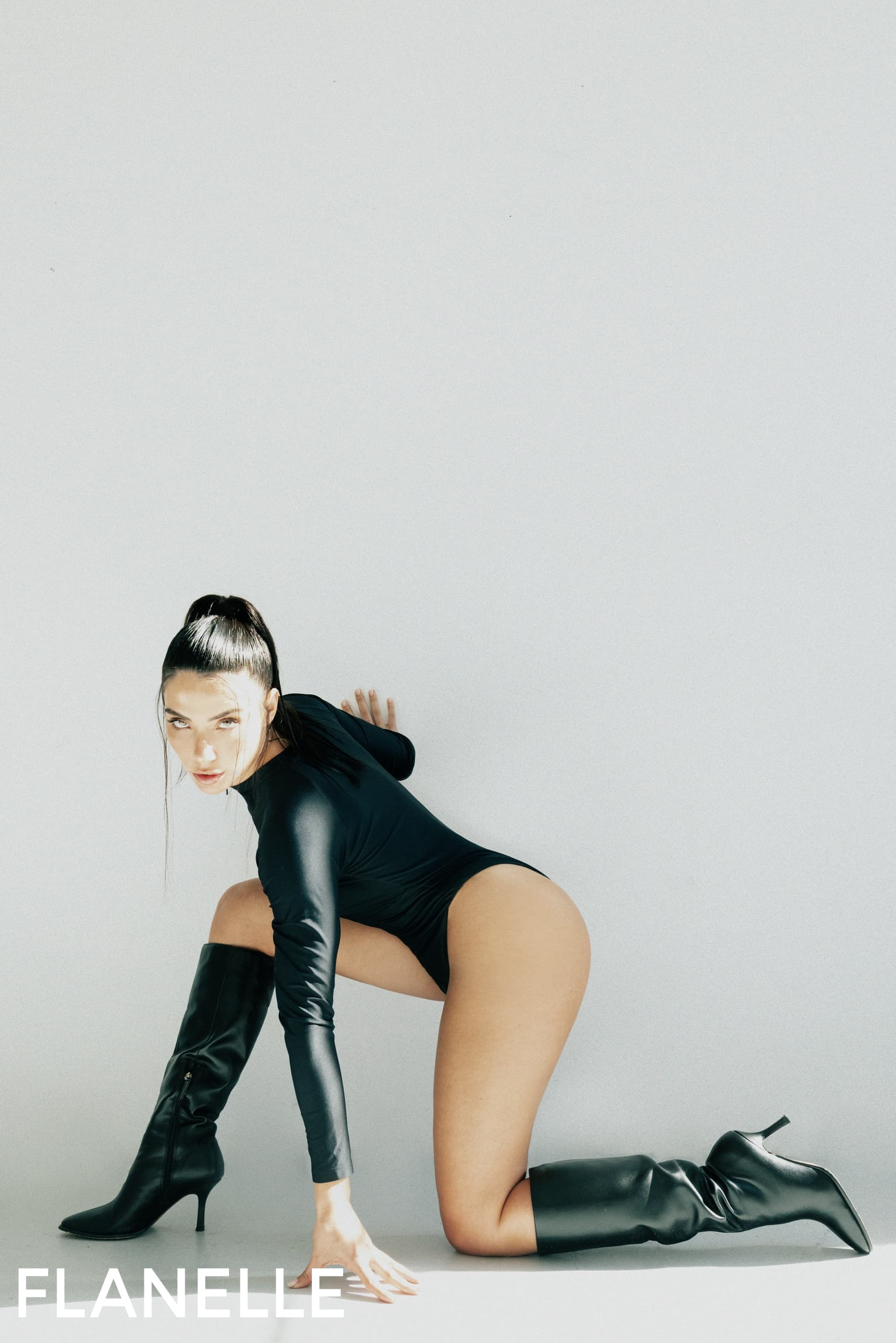 Woman in stylish black bodysuit and boots, Flanelle fashion photoshoot.