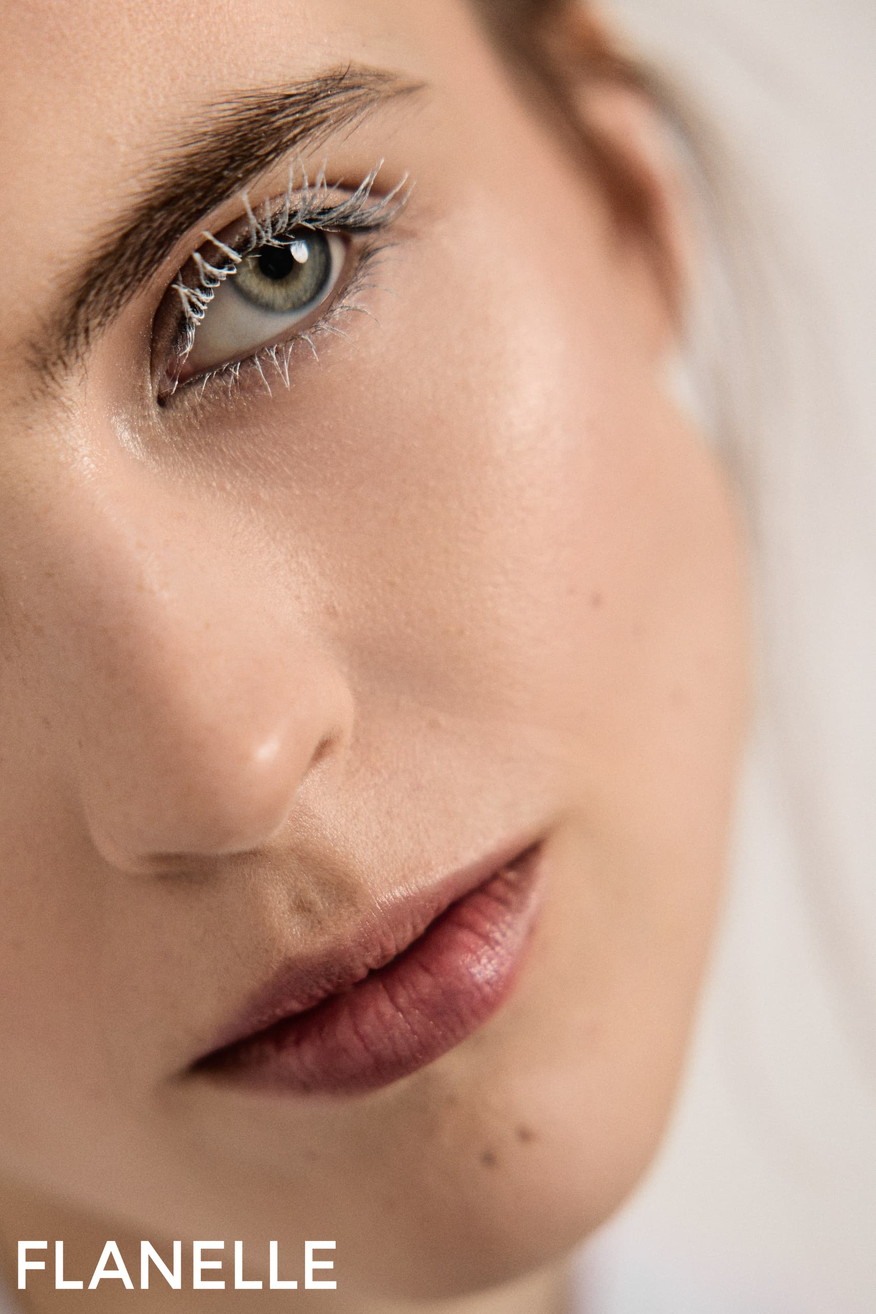 Close-up of a woman's face with bold eye makeup and natural lipstick.