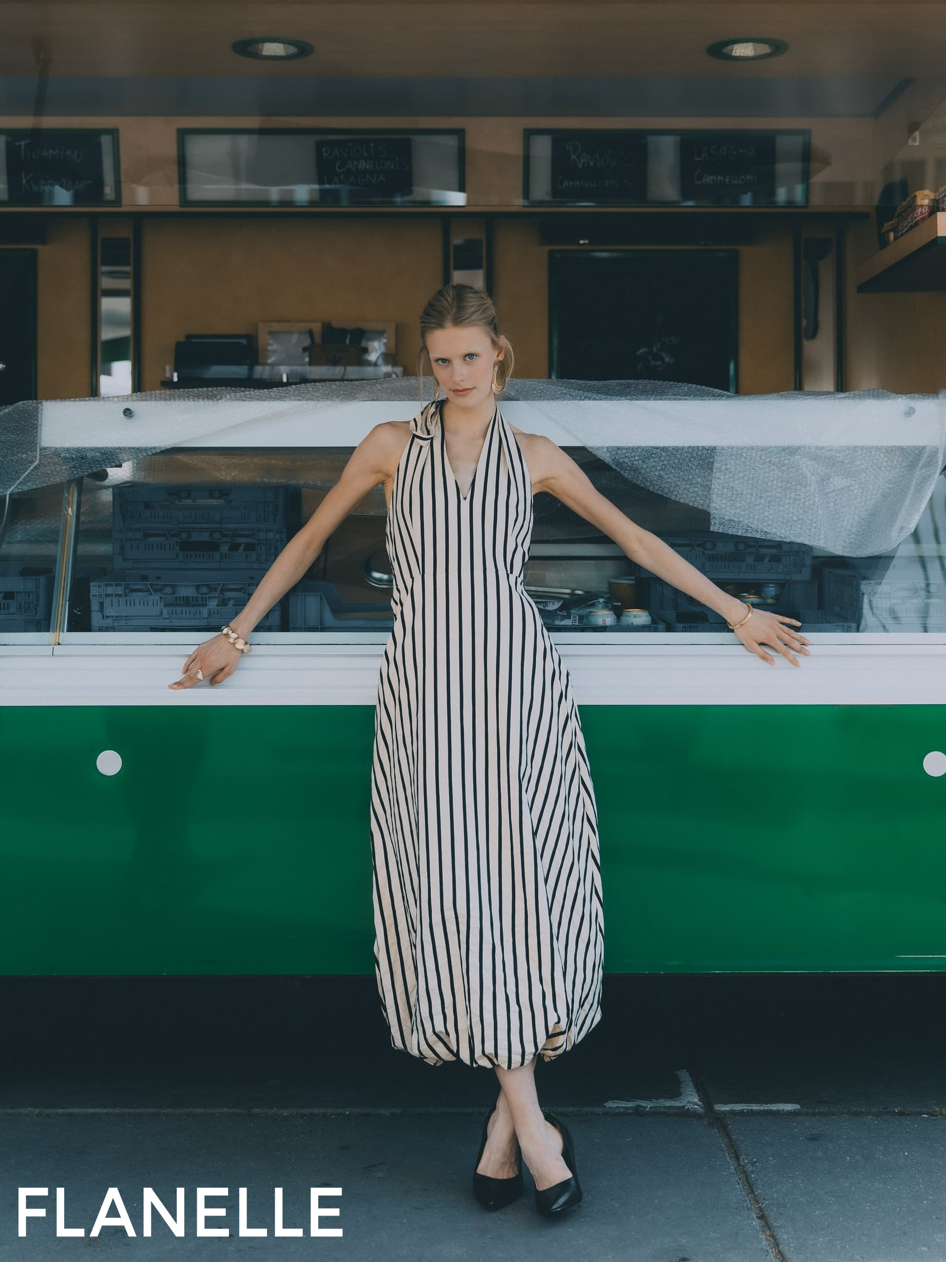 Woman in striped dress poses confidently in front of a green food truck.