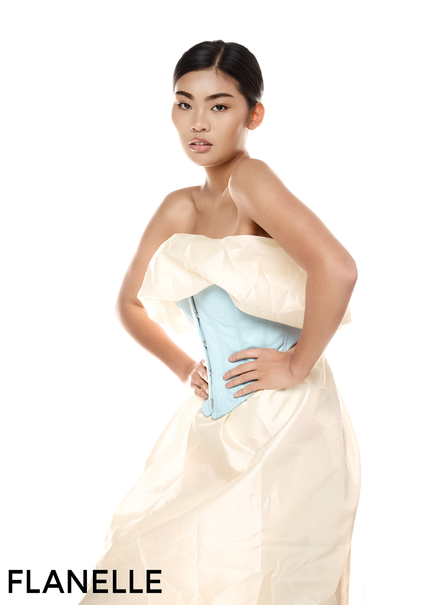 Woman in elegant dress with blue corset, posing fashionably on a white background.