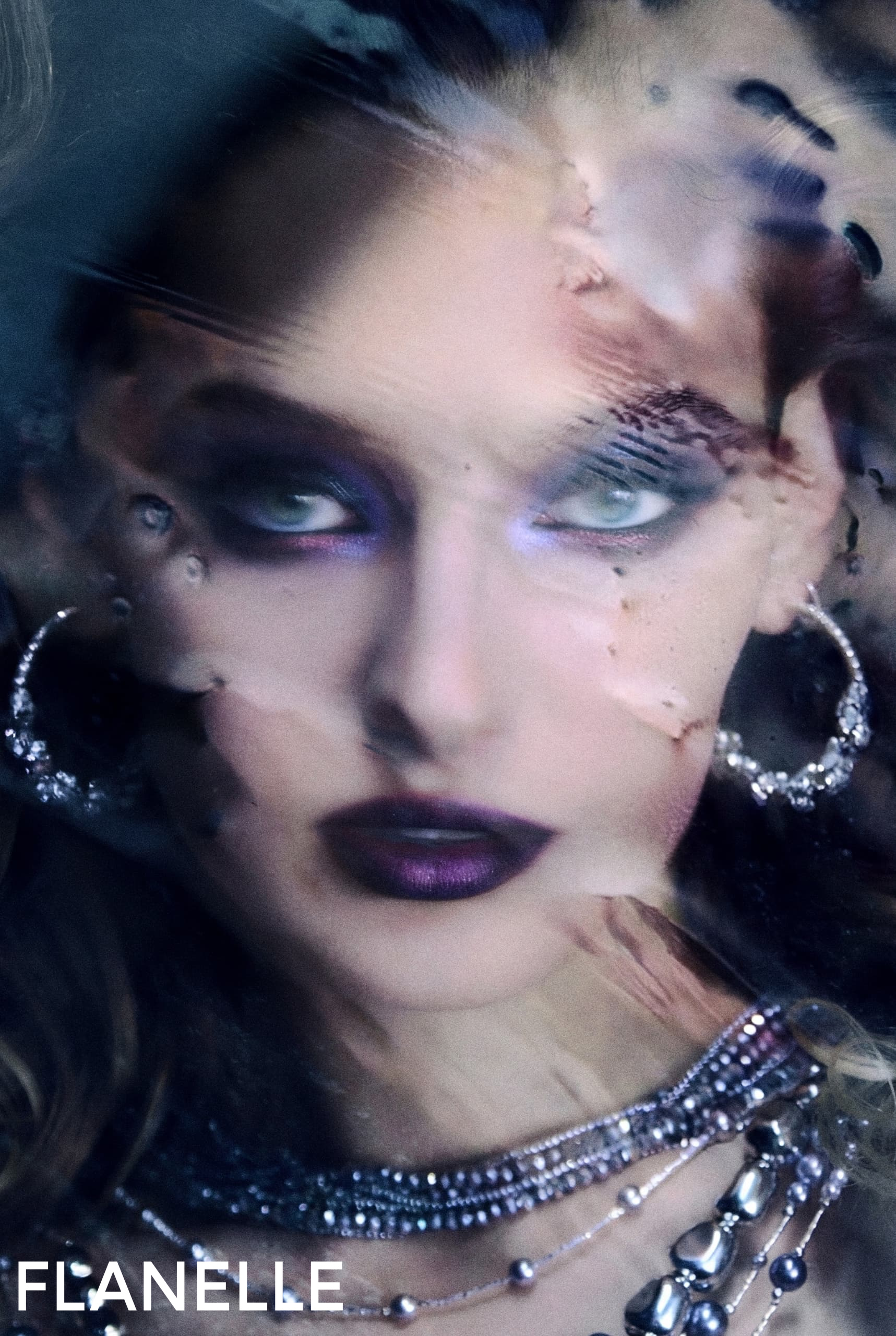Artistic portrait with bold makeup and shimmering jewelry under a textured surface.