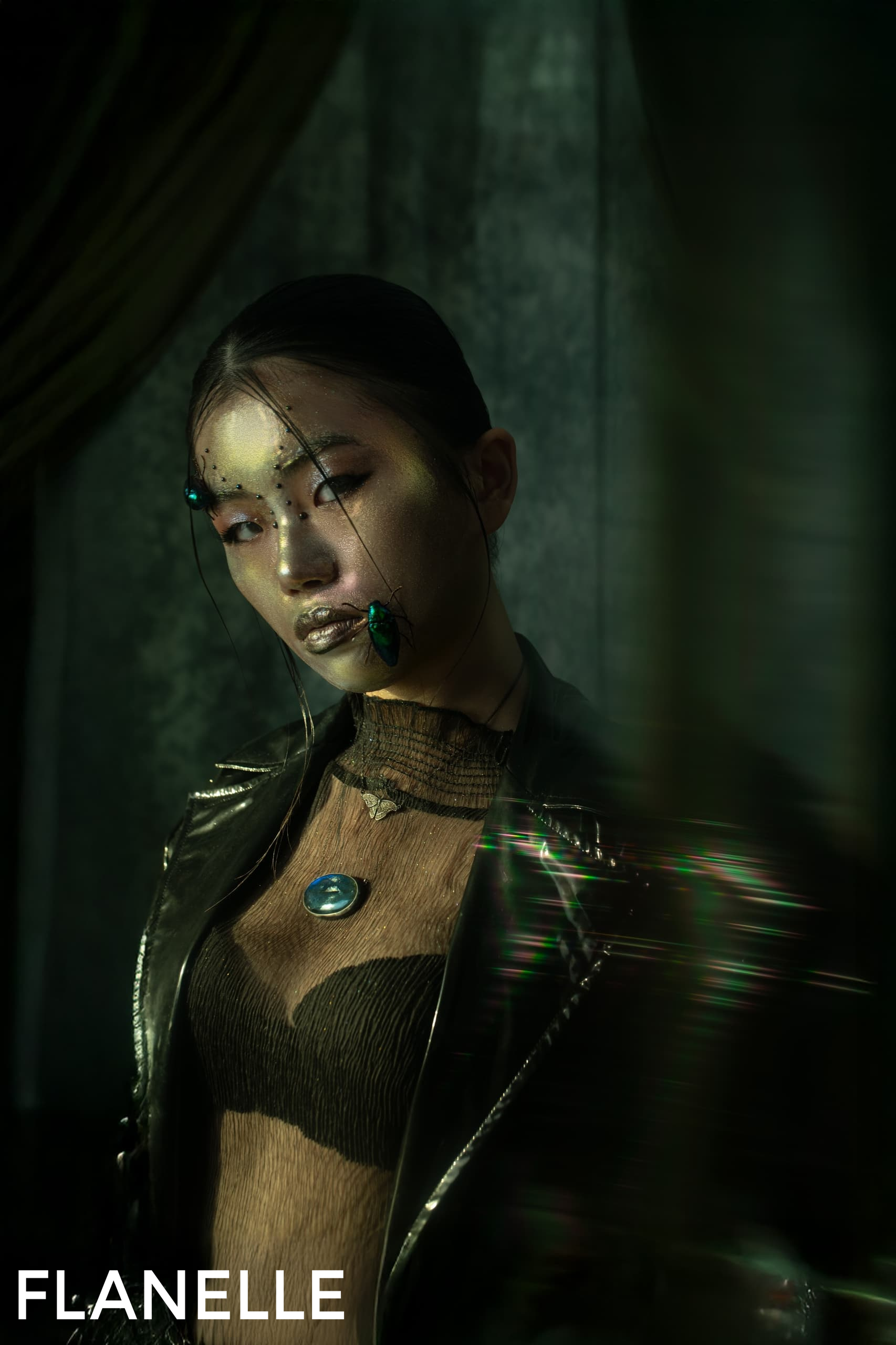 Fashion model with artistic makeup and jacket in a dramatic green setting.