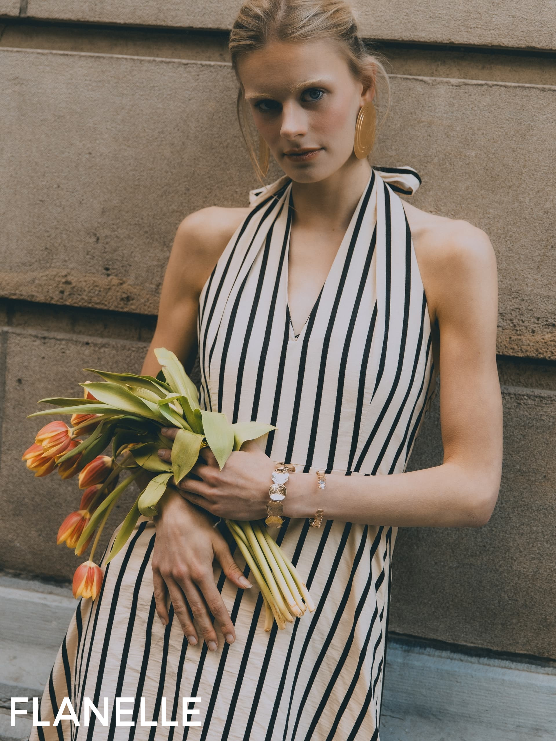 Model in striped dress holding tulips, wearing statement earrings and bracelet.