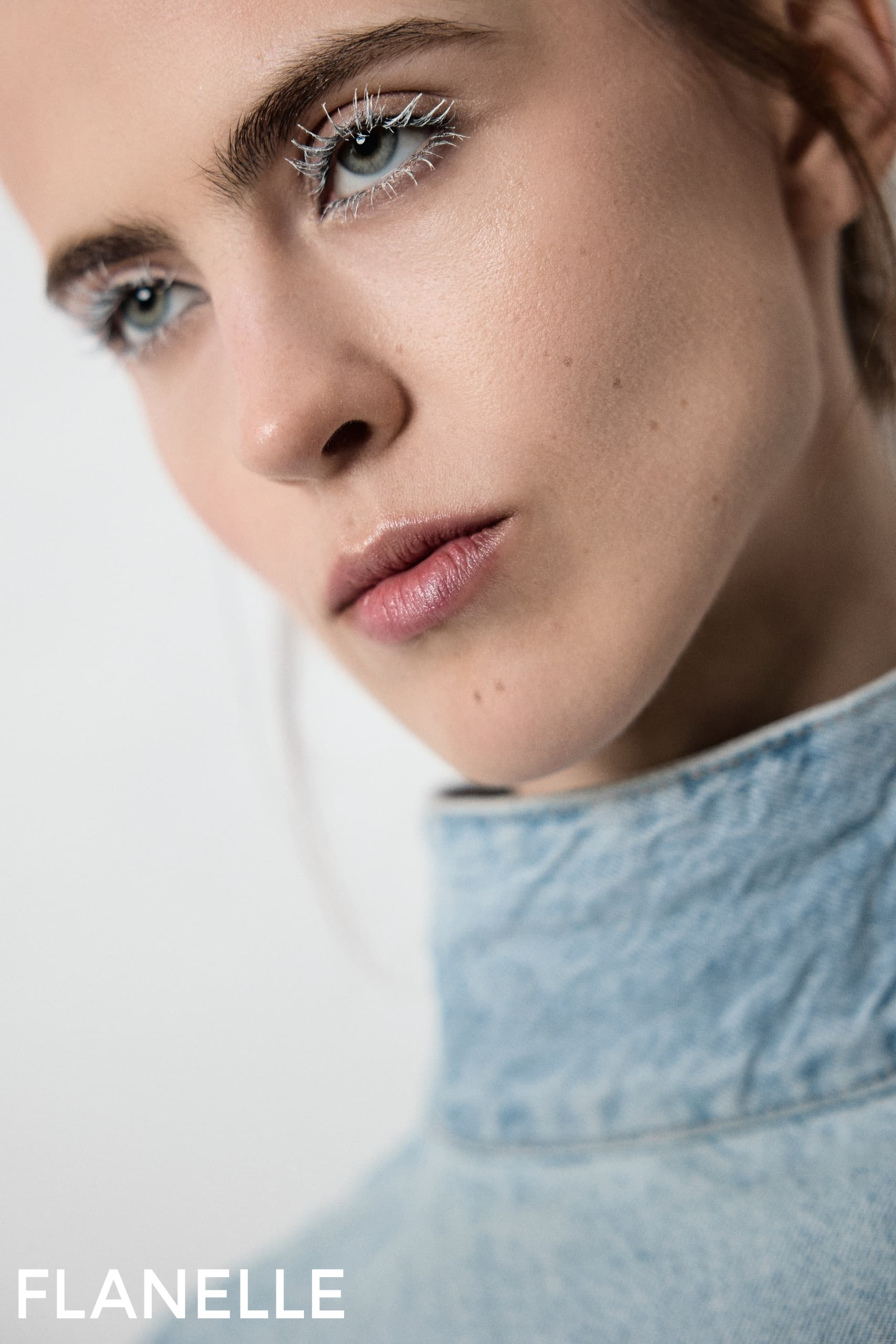 Close-up of a model with striking makeup, wearing denim by Flanelle magazine.