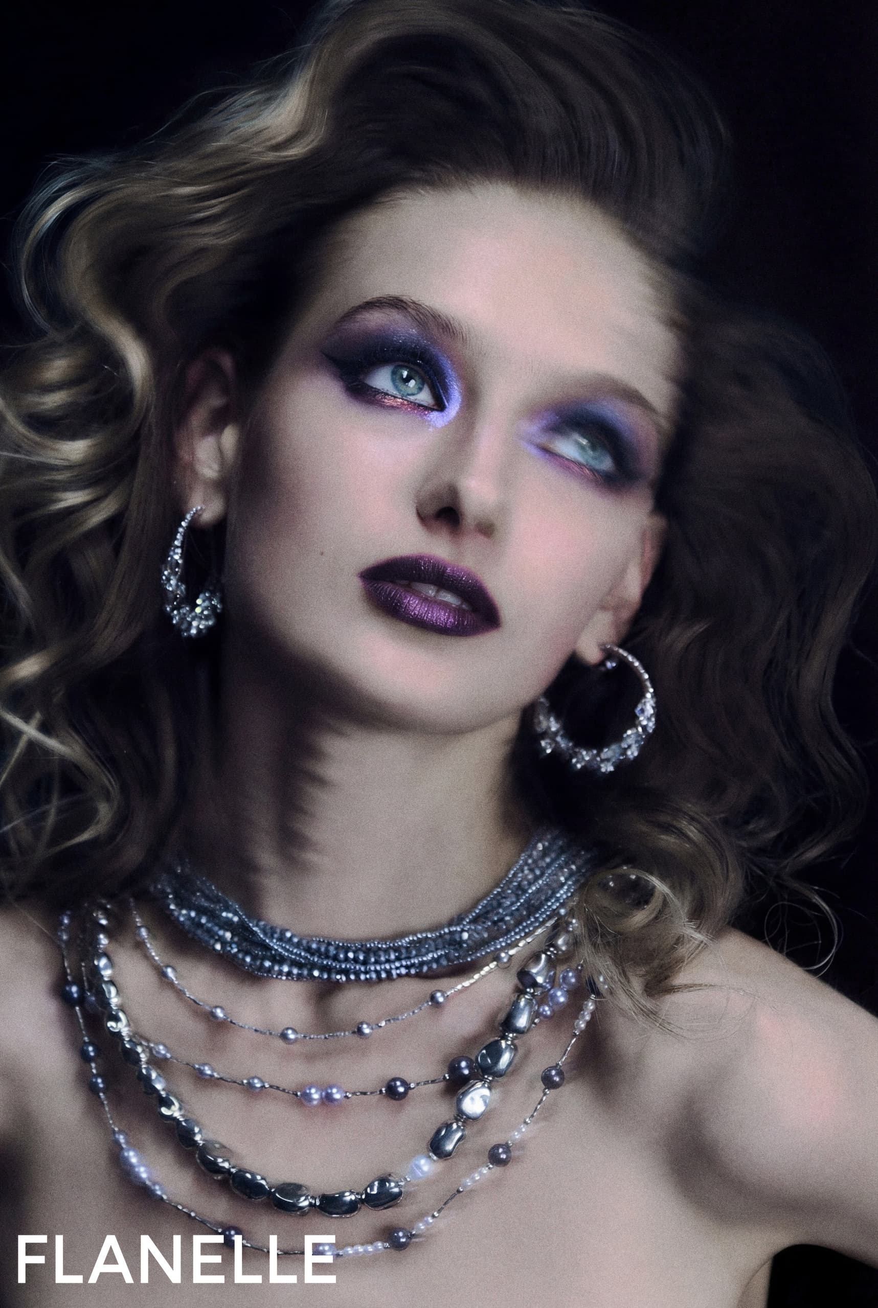 Model with bold purple makeup and layered silver jewelry, elegant fashion magazine style.