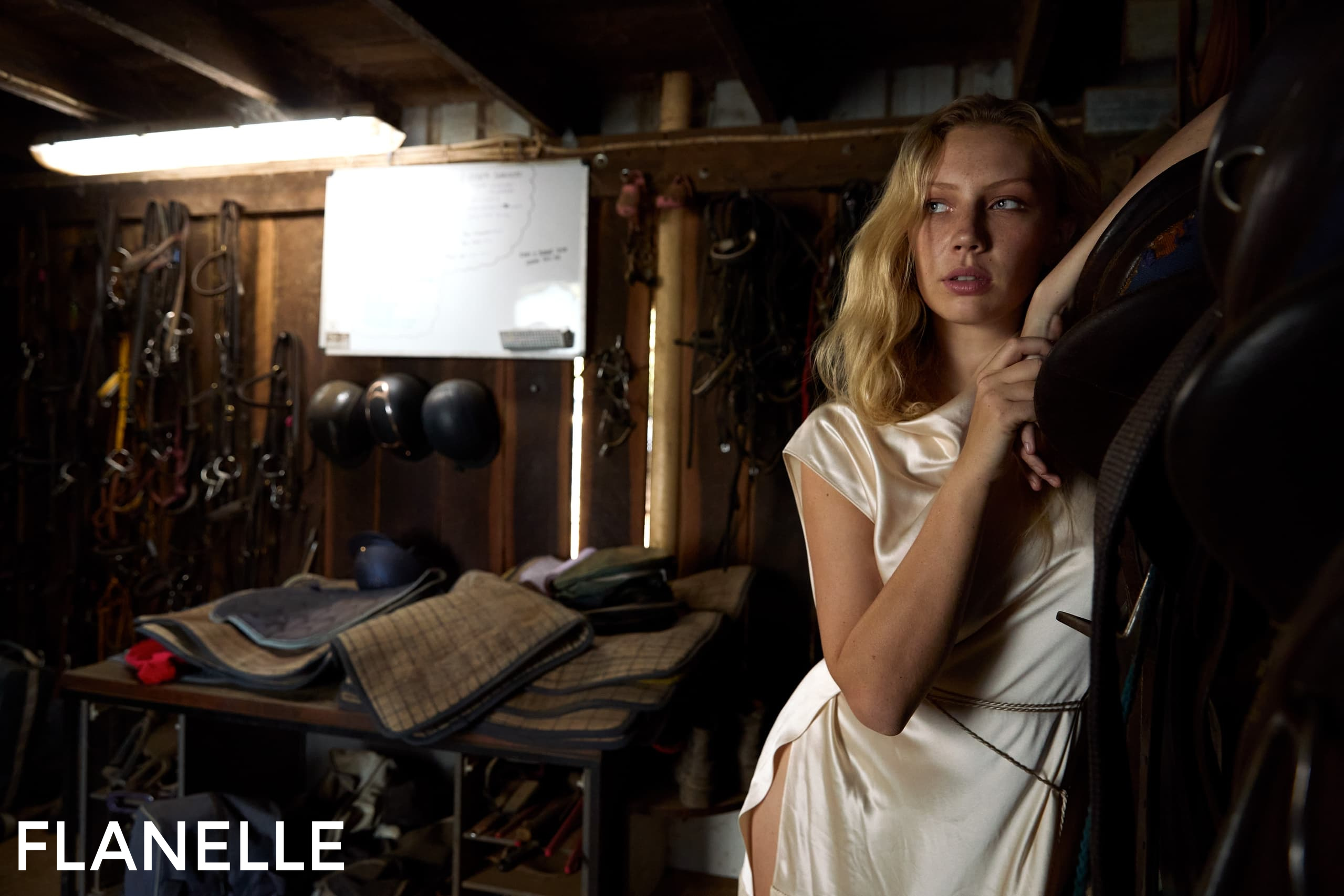 Woman in silk dress posing thoughtfully in rustic equestrian setting.