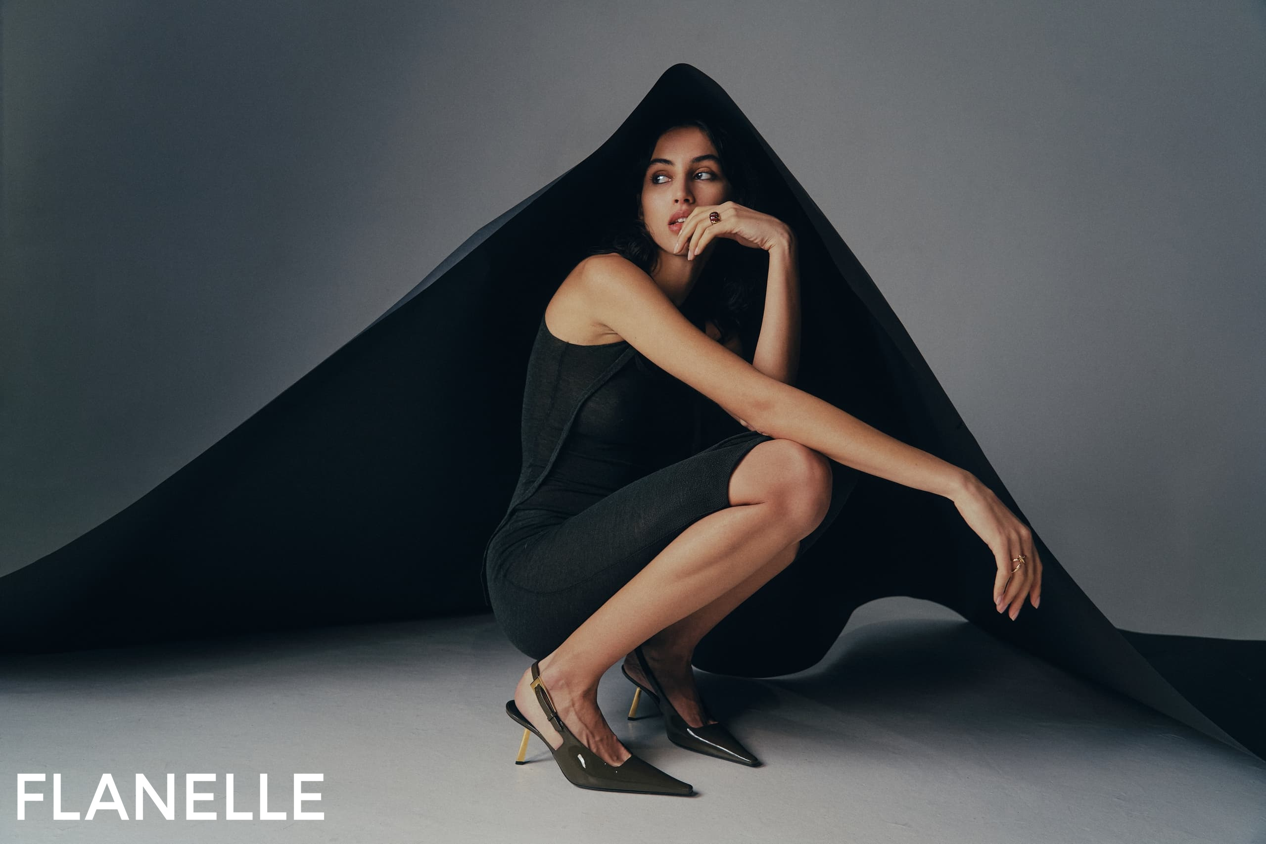 Model in elegant black outfit under artistic draped fabric.