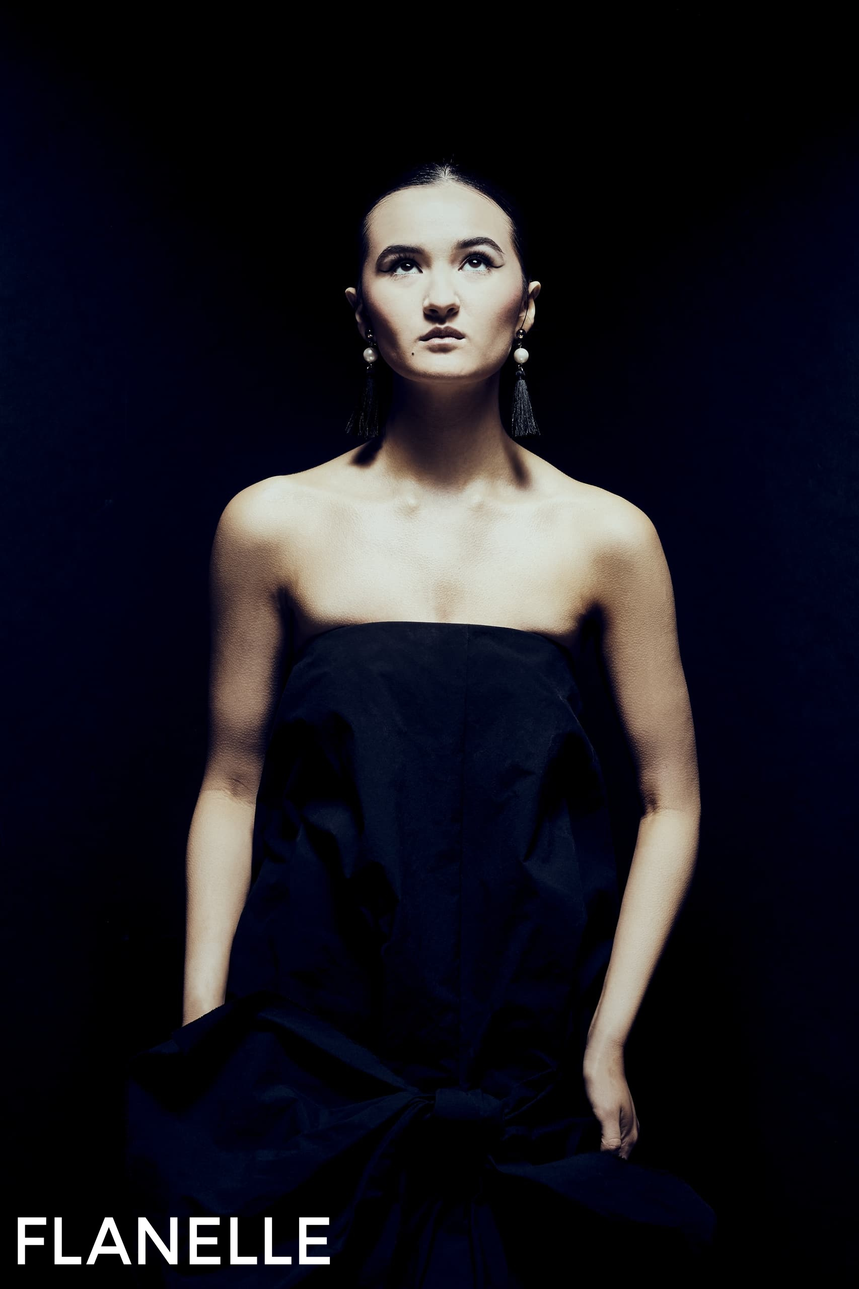 Fashion model in a strapless gown with dramatic lighting and earrings.