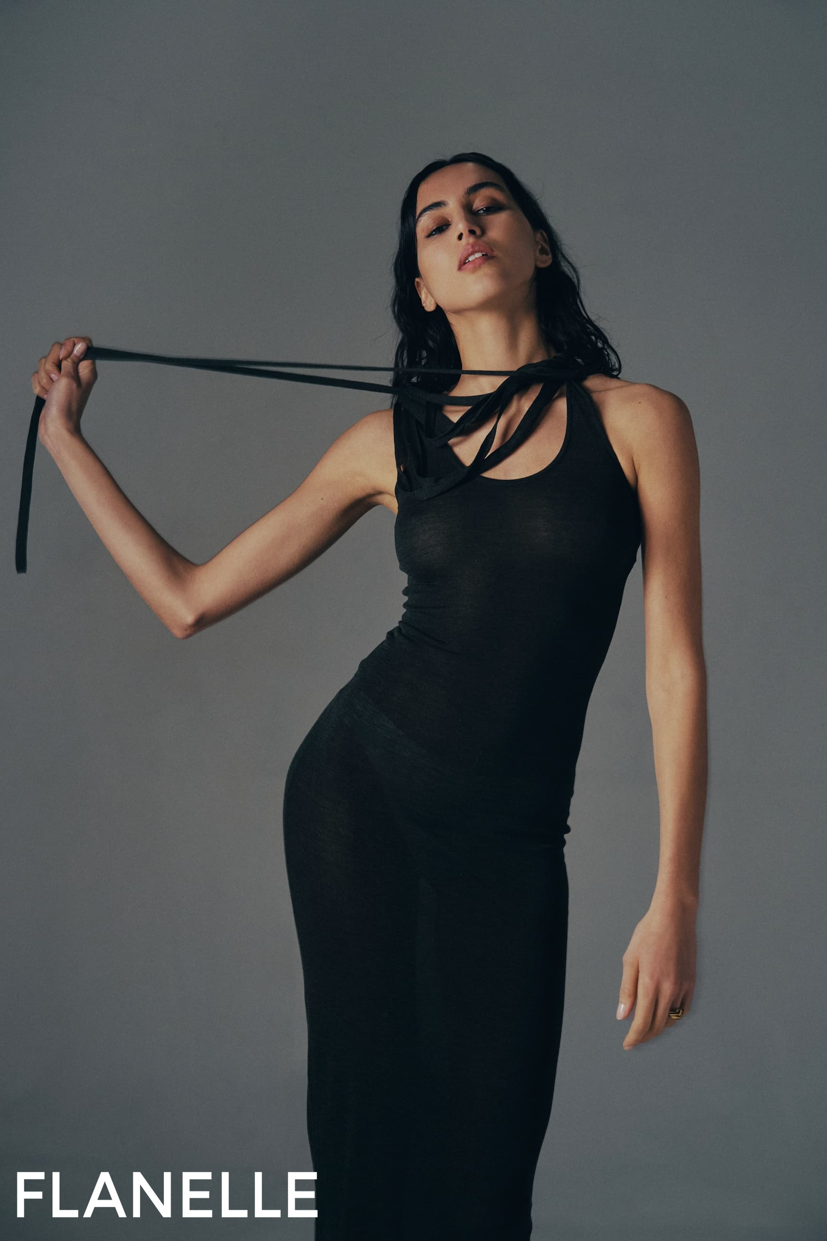 Model in black dress posing confidently with gray background.