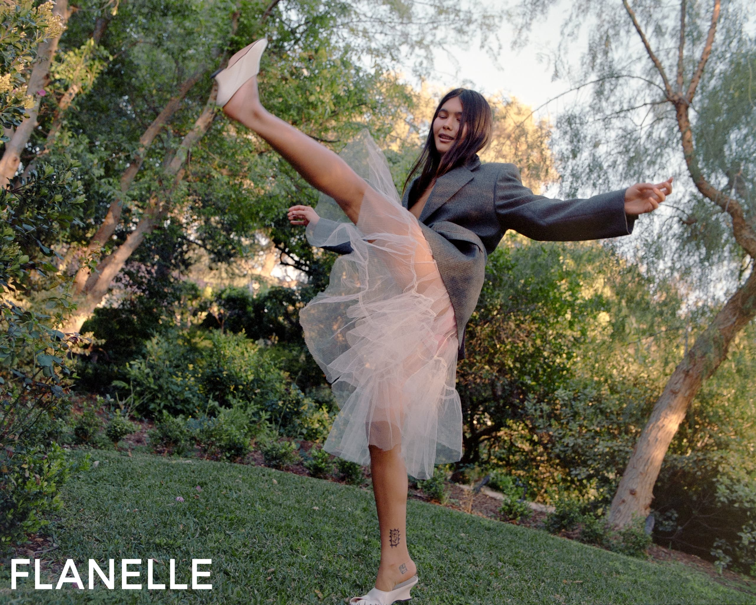 Woman dancing energetically in garden, wearing tulle skirt and oversized blazer.