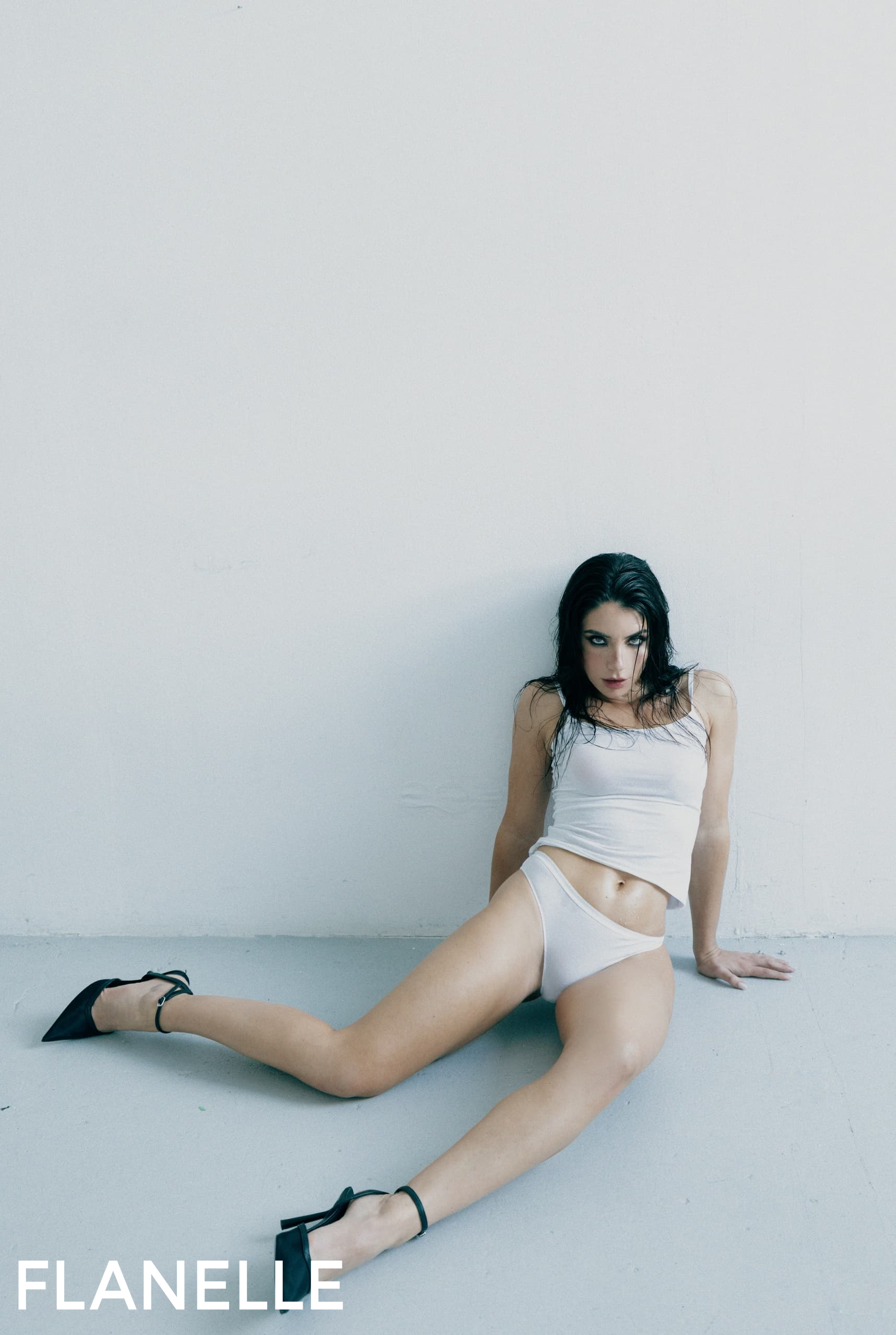 Fashion model in a minimalist pose wearing a white outfit and black heels.