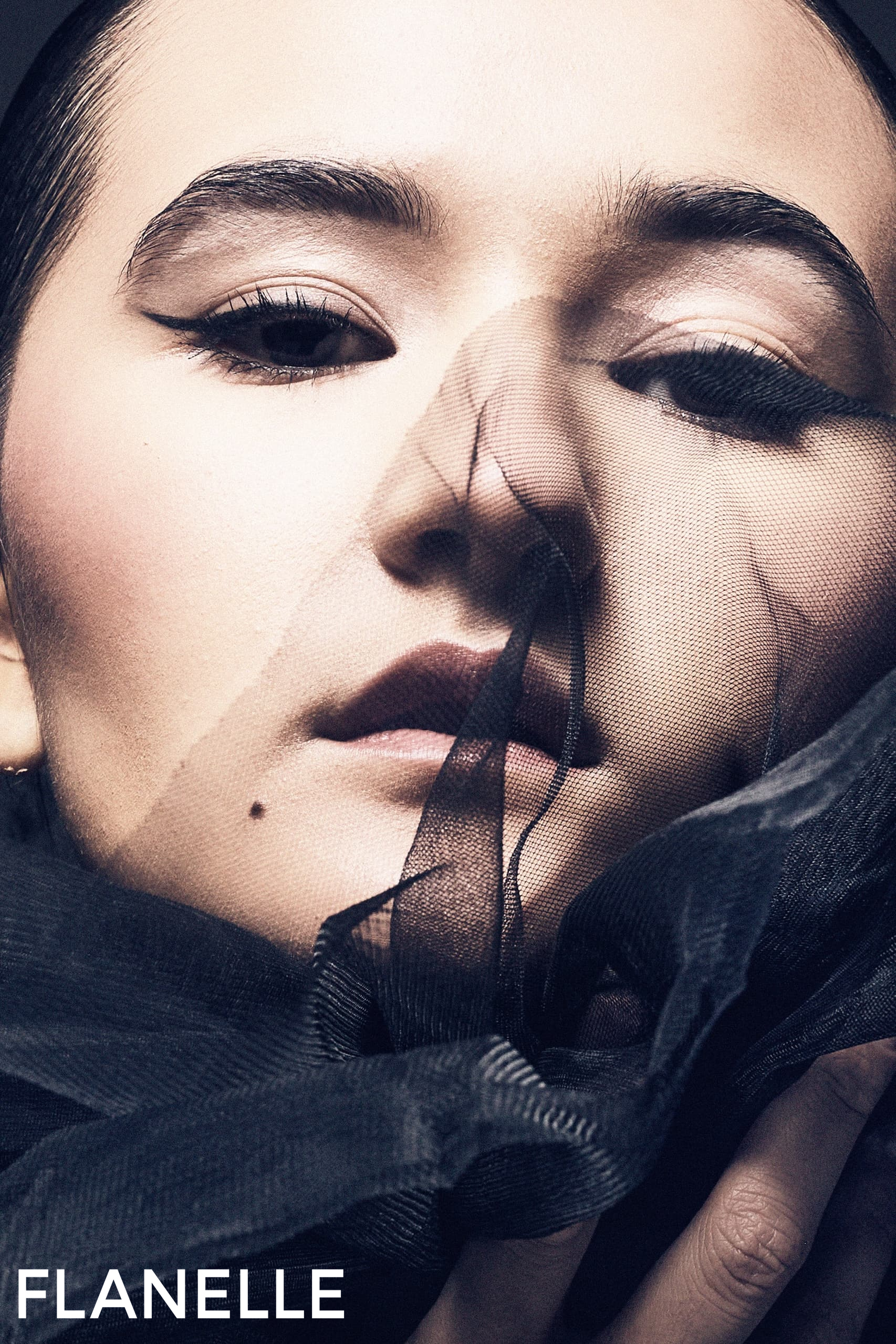 Close-up portrait with black sheer fabric veil, dramatic makeup, fashion elegance.