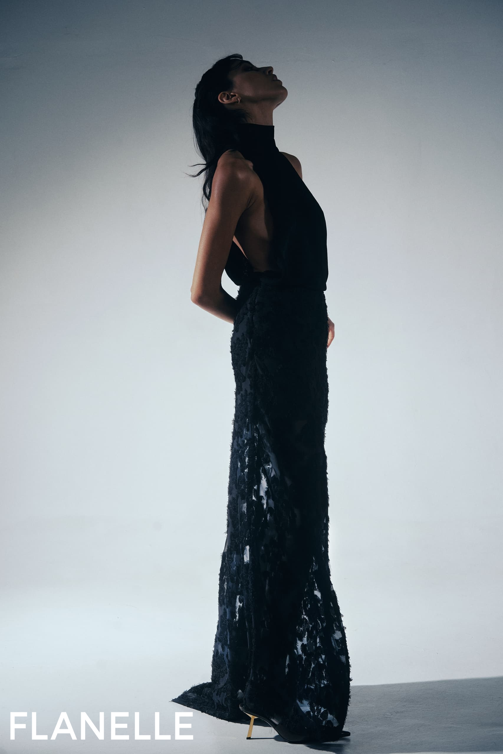 Elegant woman in black evening gown poses gracefully in a minimalist setting.
