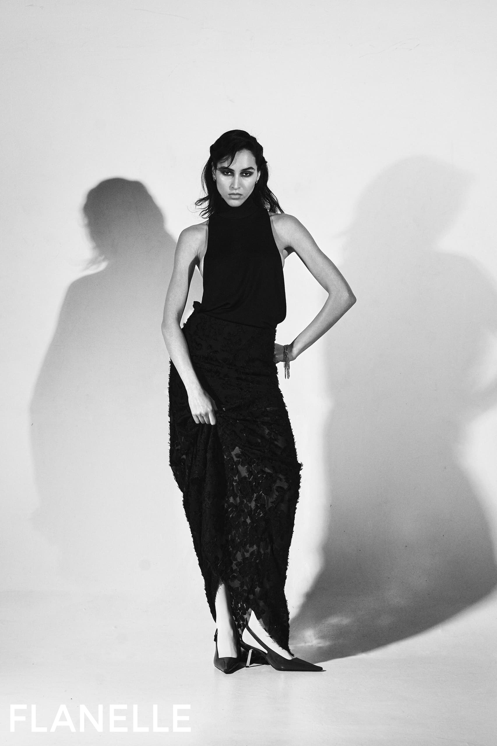 Woman in black halter dress striking a confident pose in a studio setting.