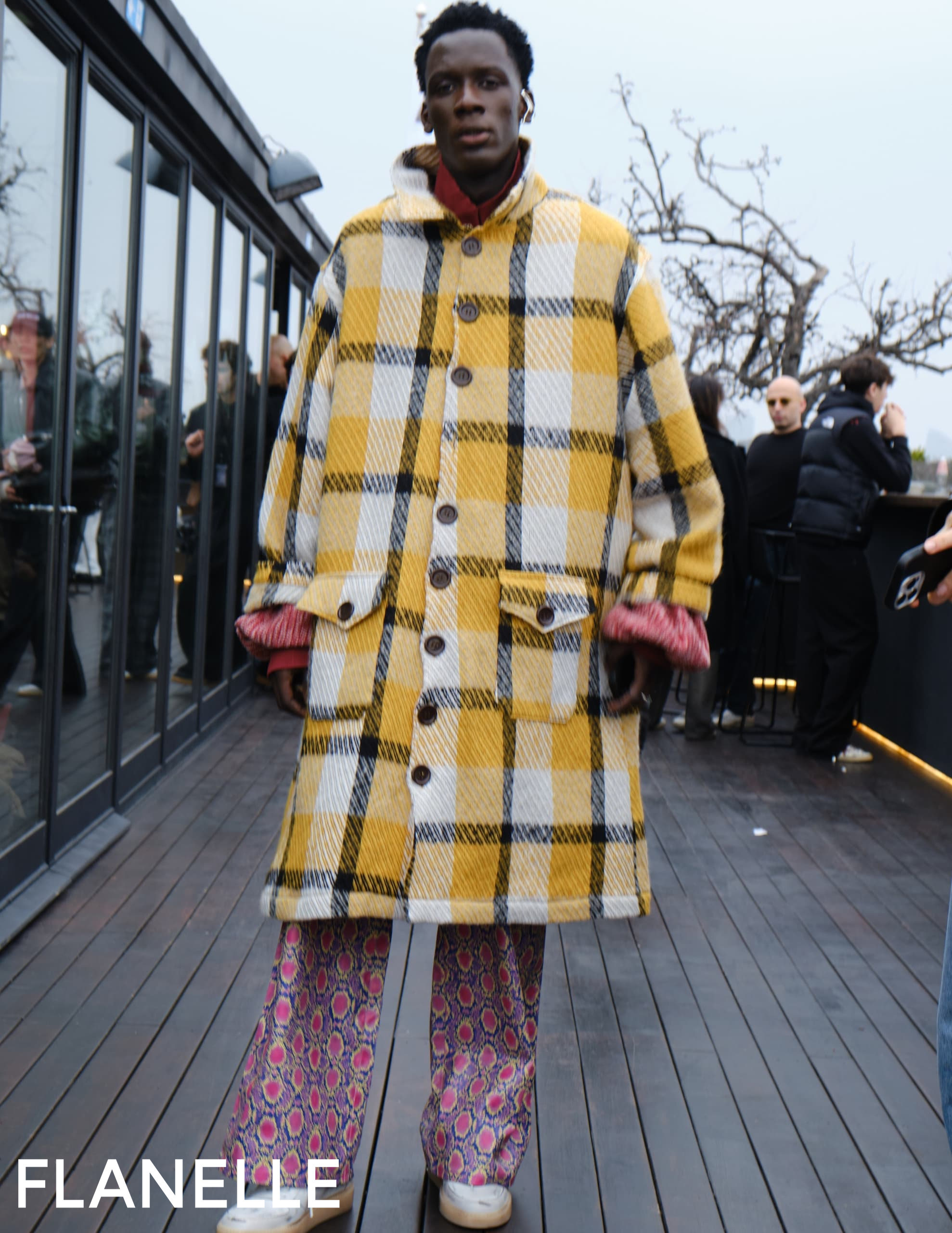 Fashion-forward individual in plaid coat on an outdoor terrace.
