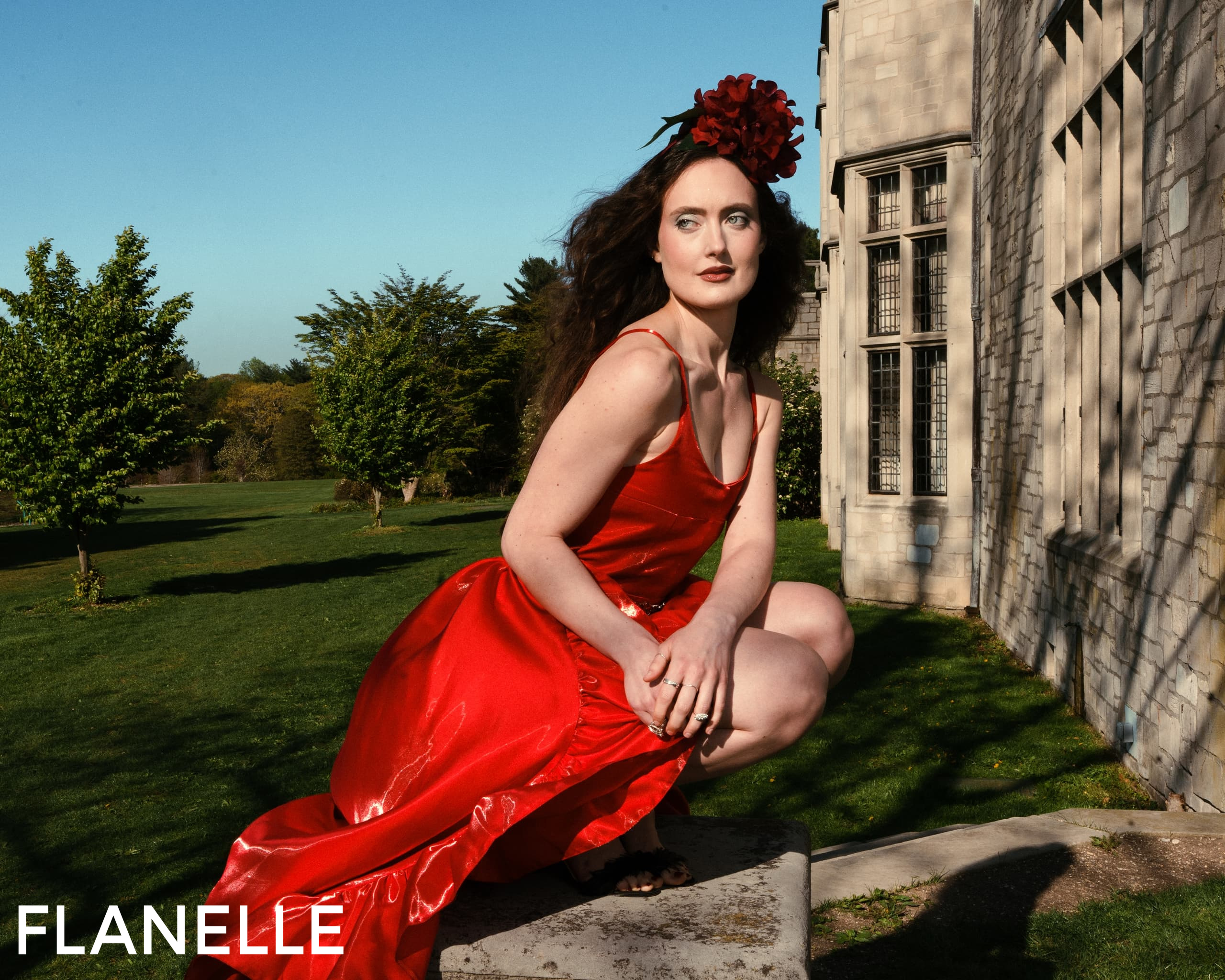 Woman in elegant red dress poses gracefully outside a stone building.