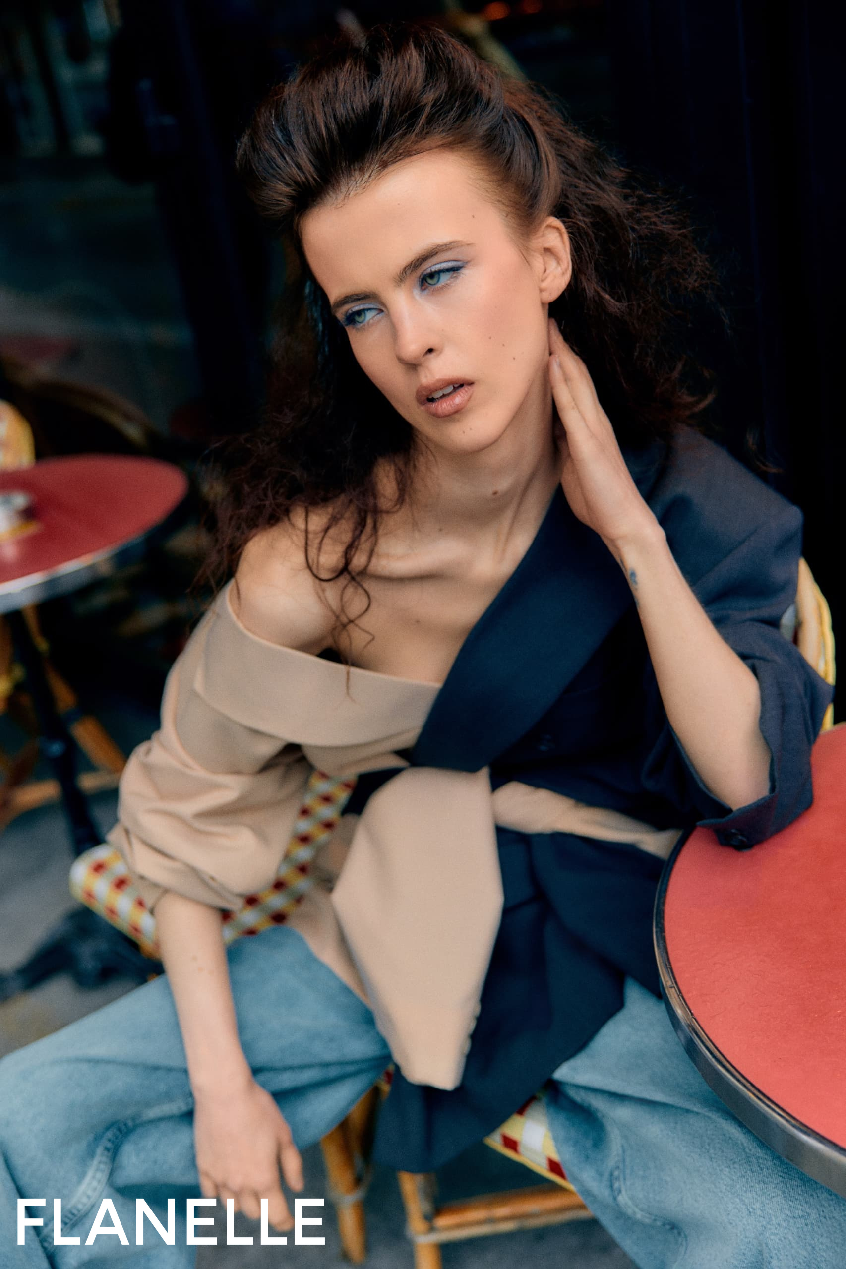 Fashion model with stylish outfit and makeup seated at a café table.