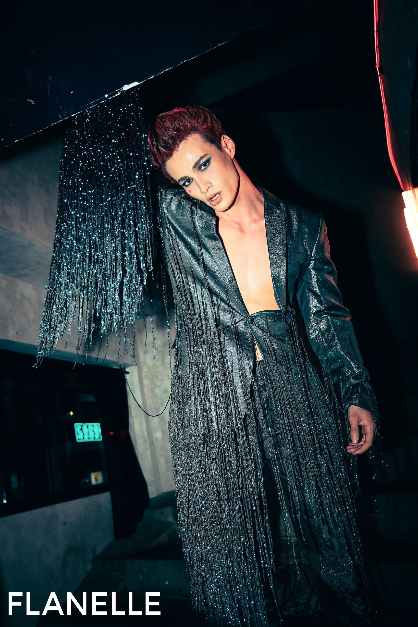 Fashion model in a bold, shimmering outfit with fringe, posing dramatically.