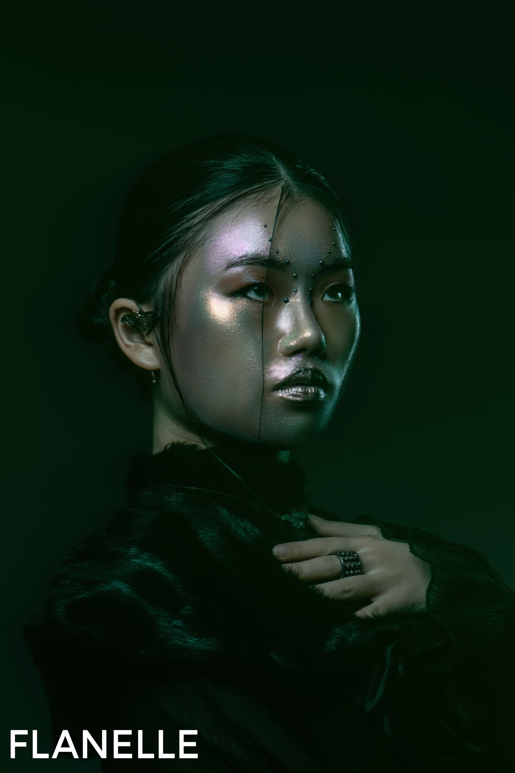 Futuristic fashion model with sparkling makeup and dark attire under green lighting.