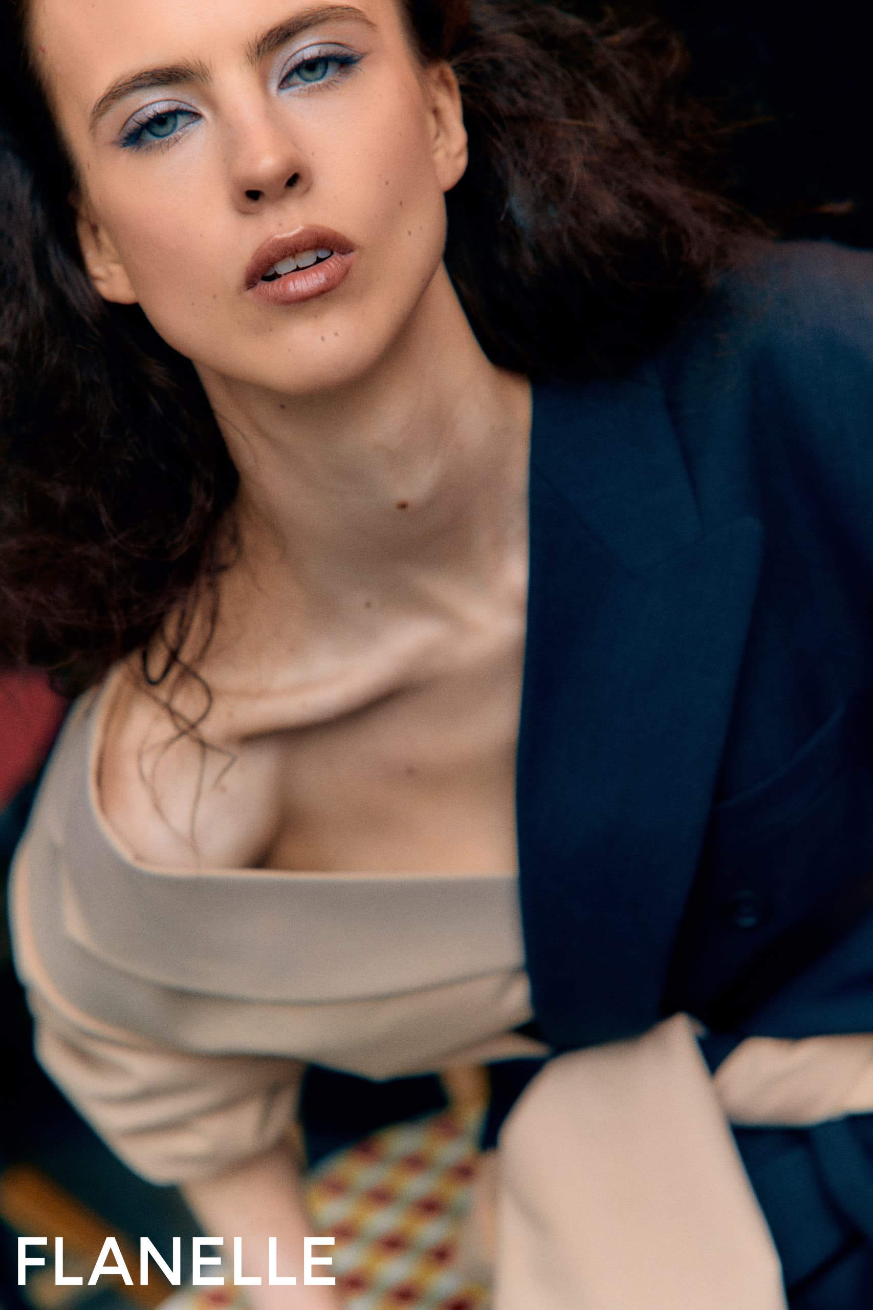 Stylish model in blue blazer and beige top with striking blue eyeshadow.