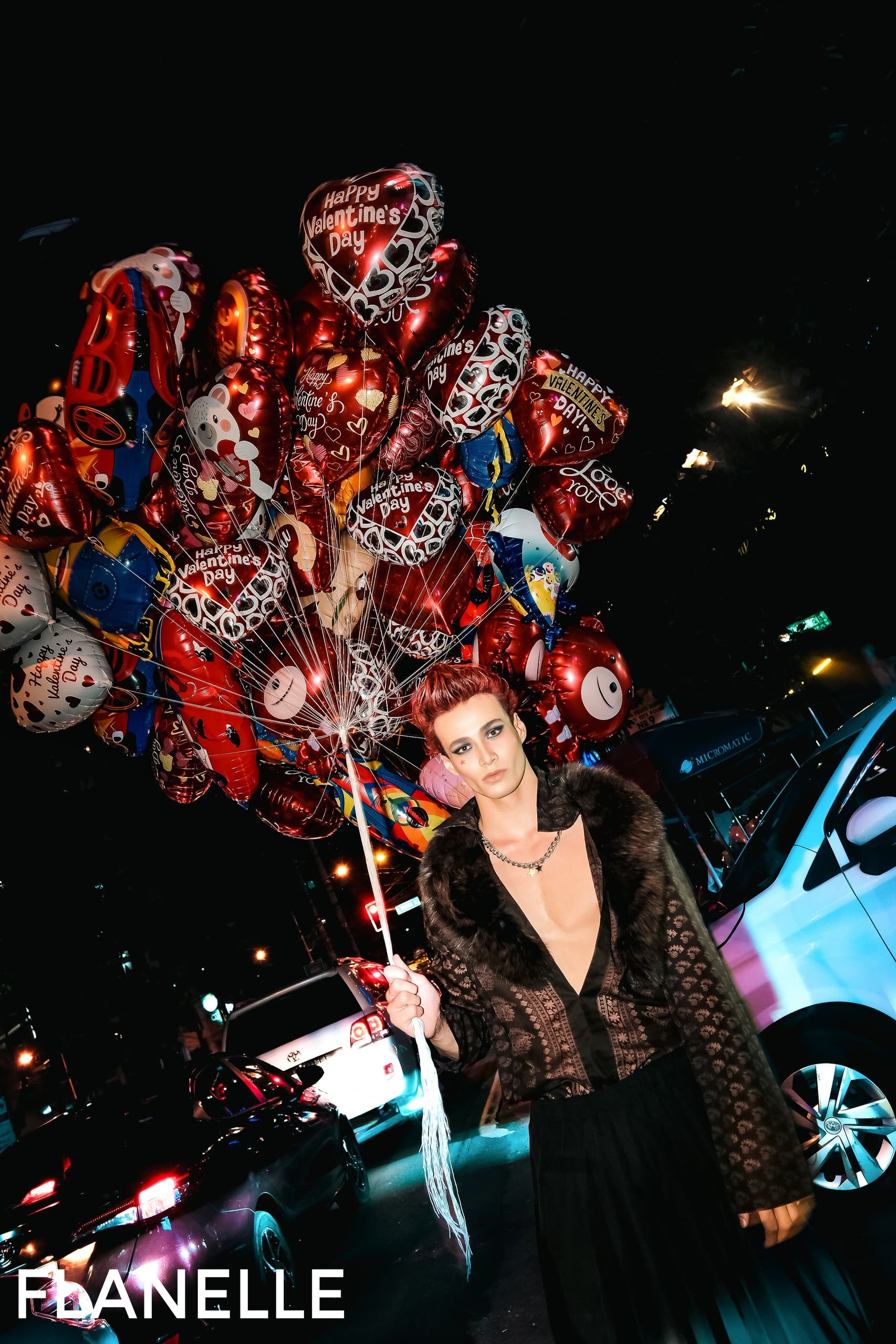 Person with Valentine's balloons on city street at night. Stylish outfit, festive scene.