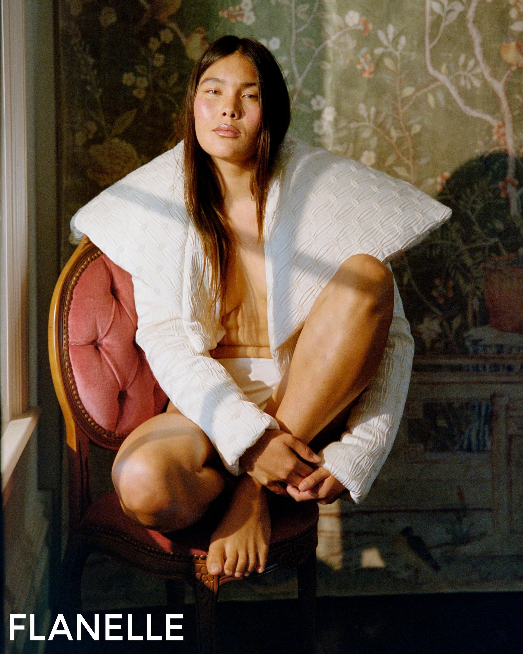 Person in textured white jacket sitting on chair, artistic floral background.