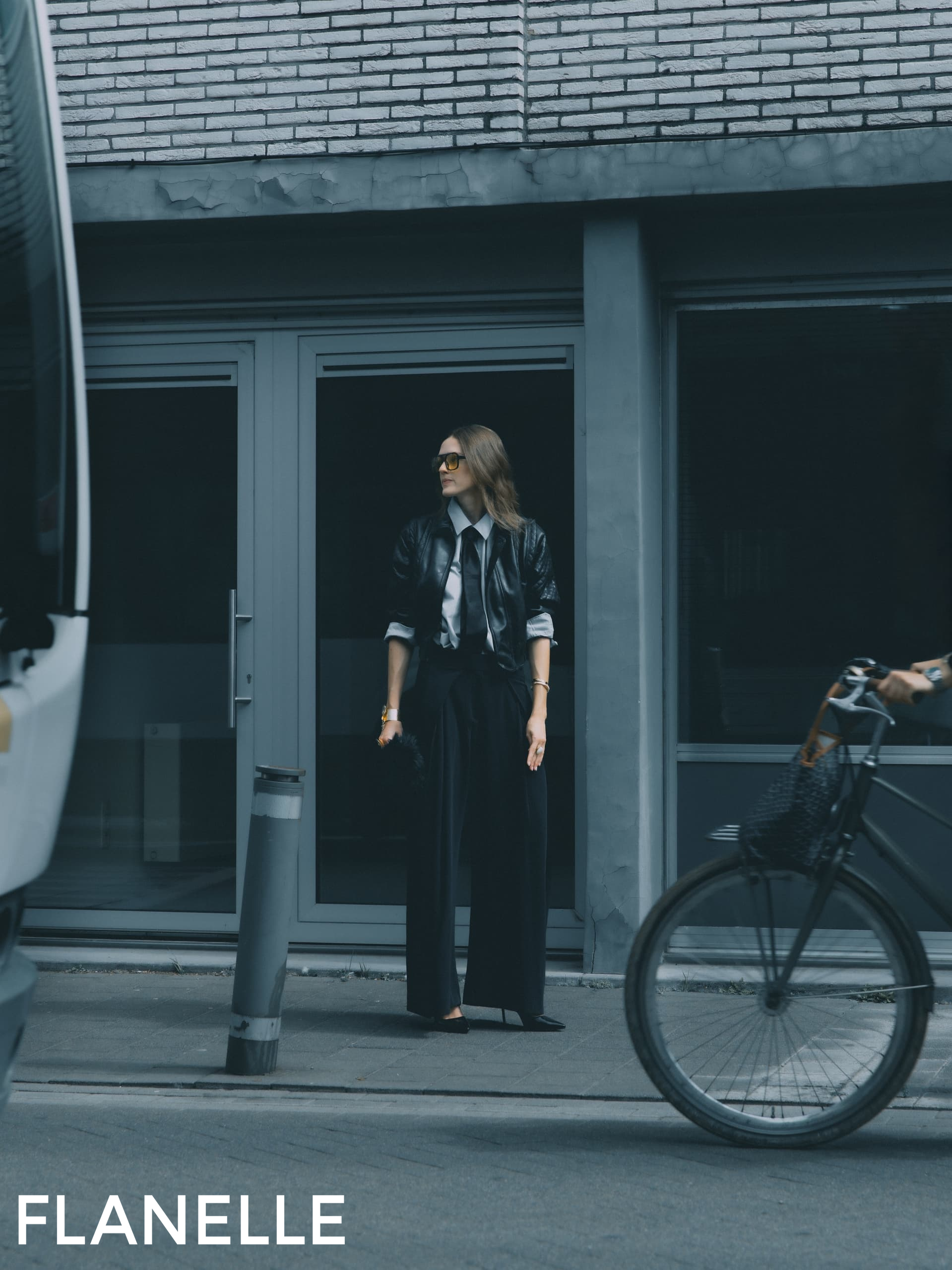 Stylish woman in sunglasses stands on city street, bike passing by.