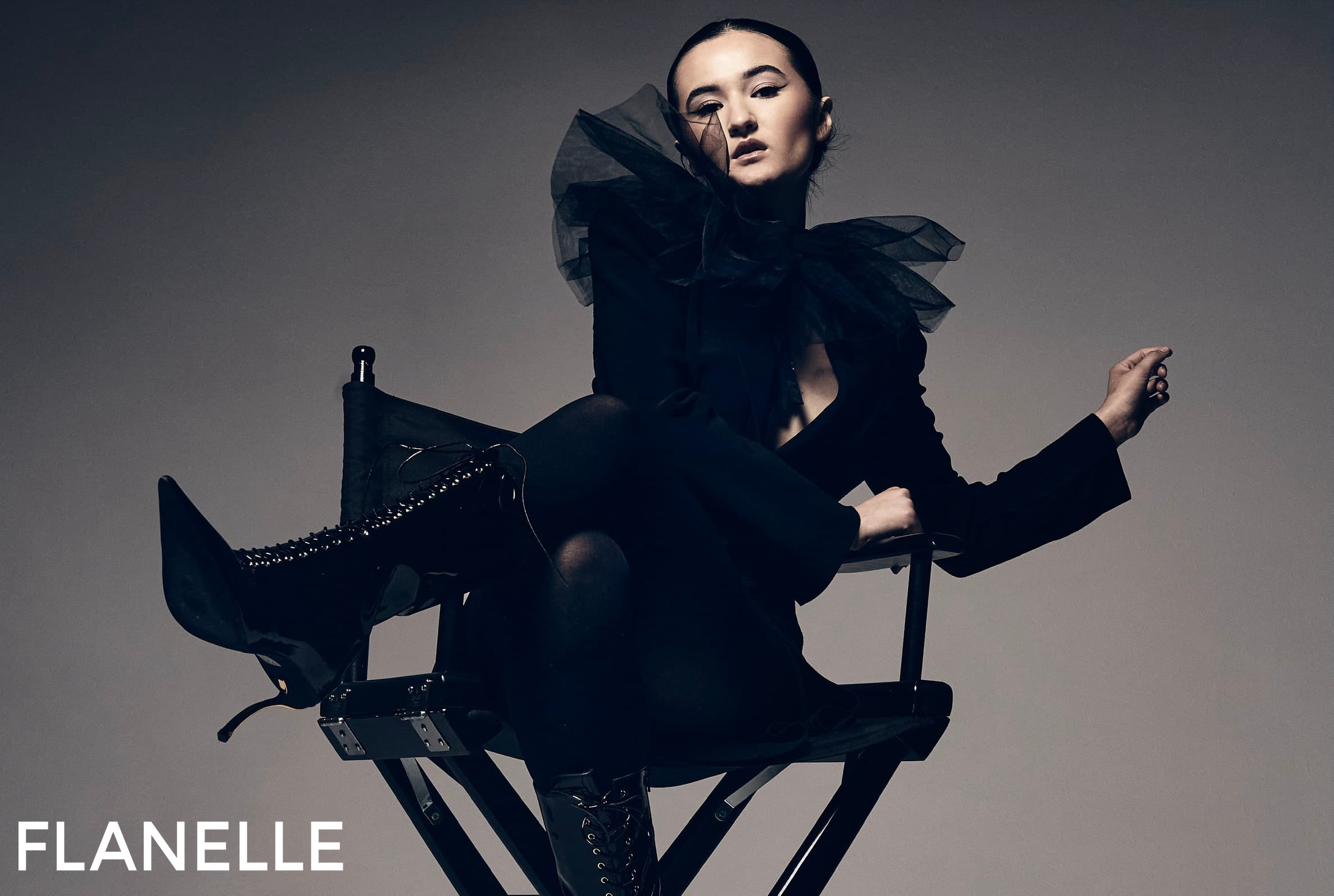 Fashion model in striking black attire, sitting stylishly on a chair.