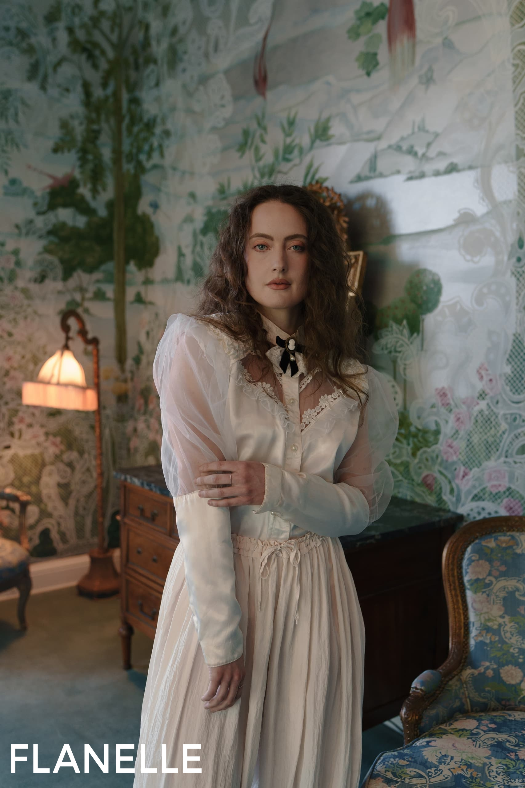 Woman in vintage white dress in elegant, floral-themed room, with soft lighting.