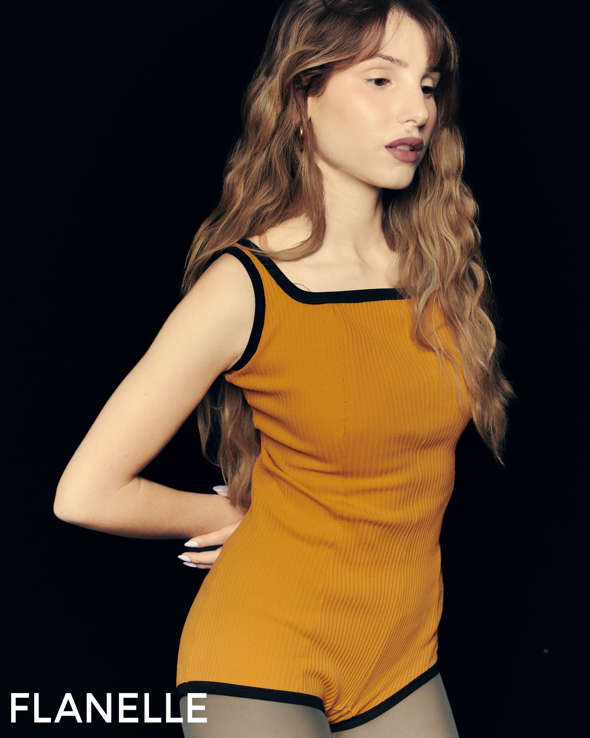 Woman in stylish mustard outfit against black background.