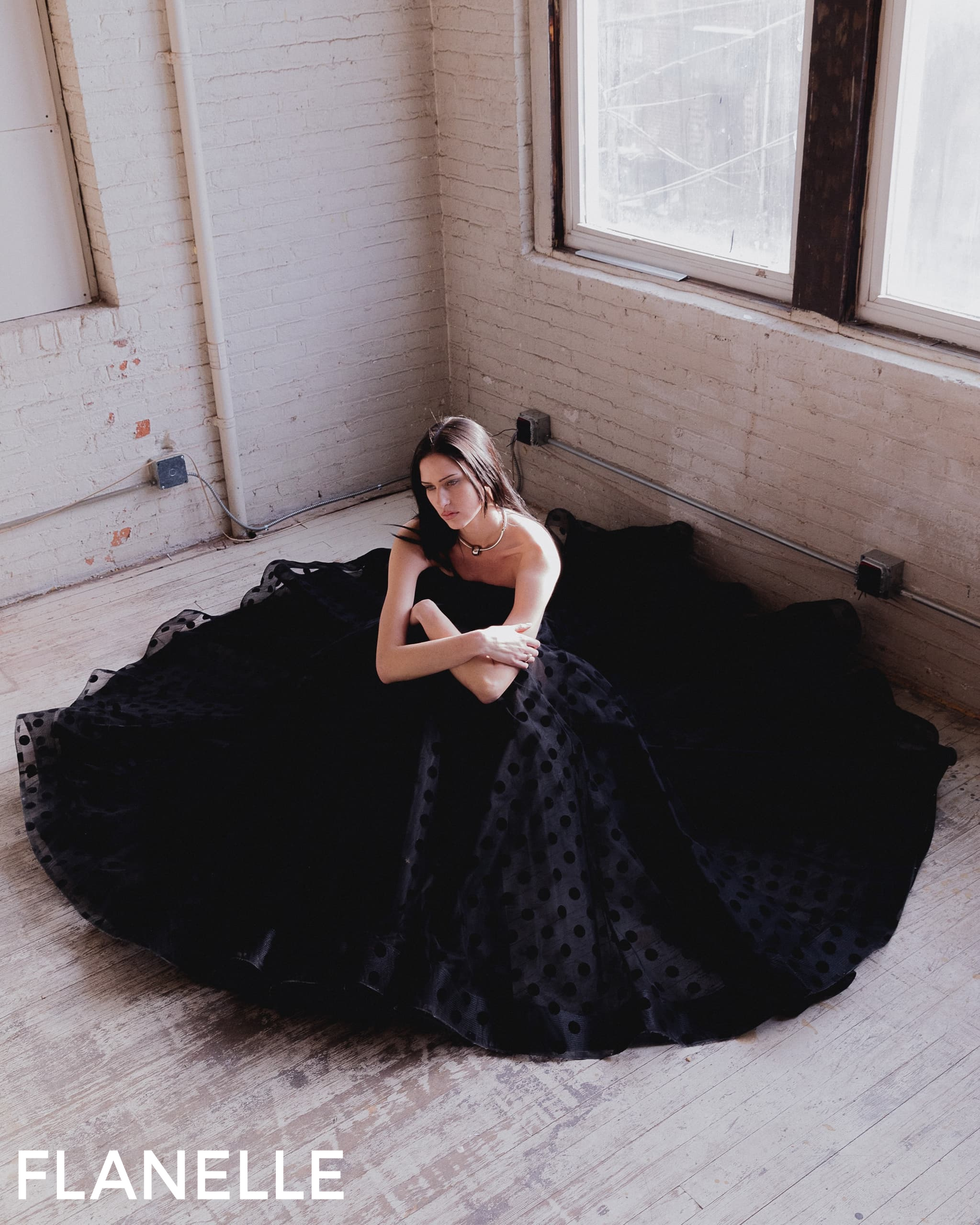 Woman in black polka dot dress sitting on floor by window.