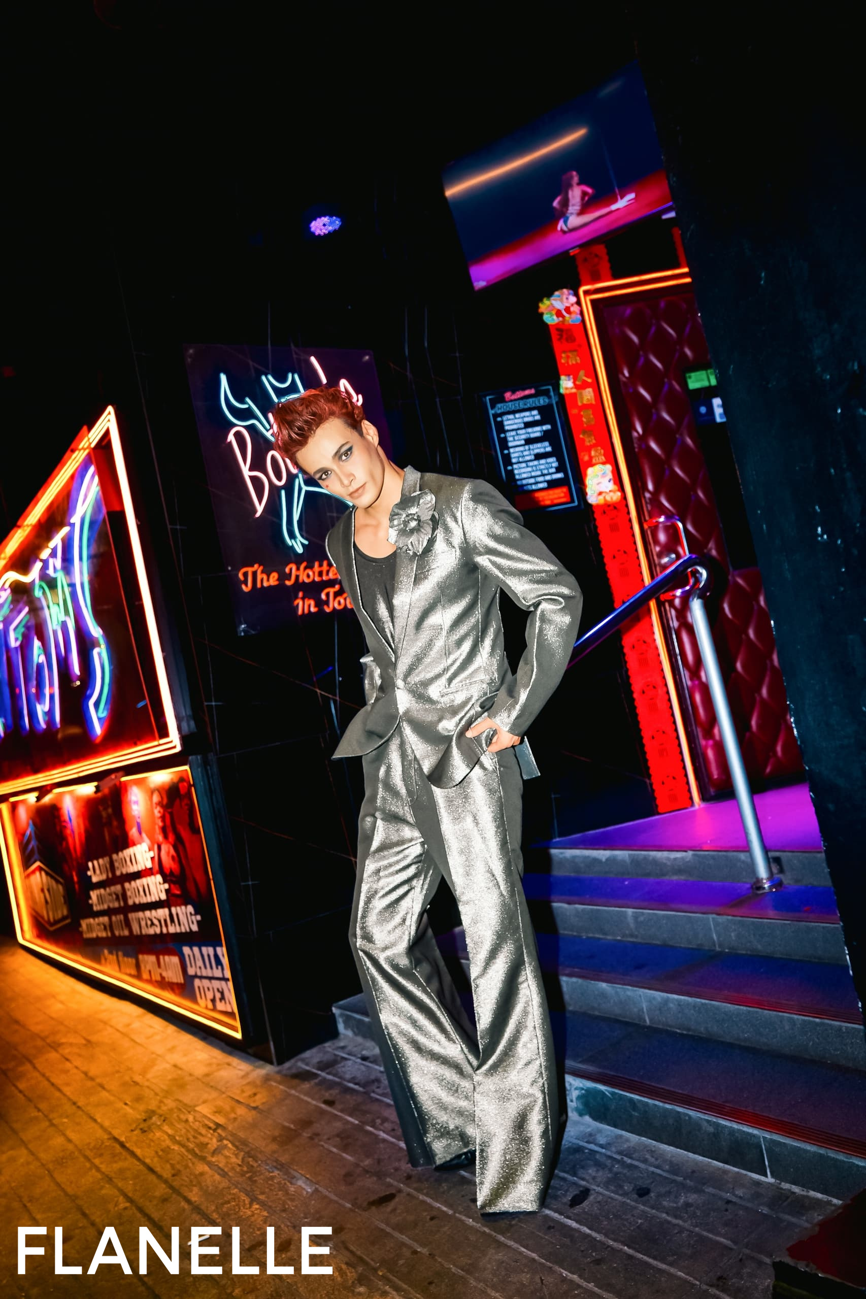 Person in a silver suit posing in a vibrant, neon-lit interior.