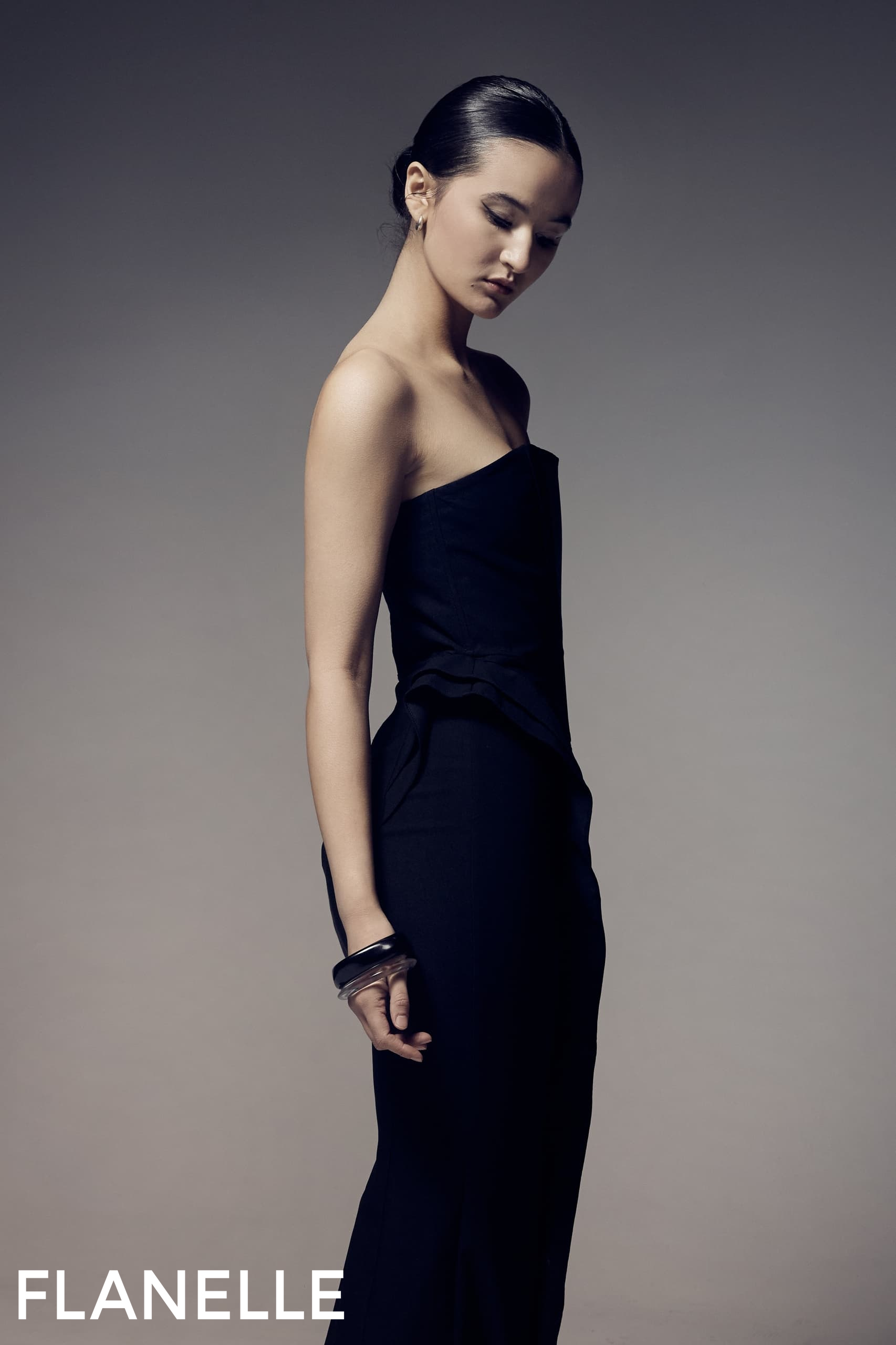 Elegant woman in a strapless black dress, posing for a fashion photoshoot.