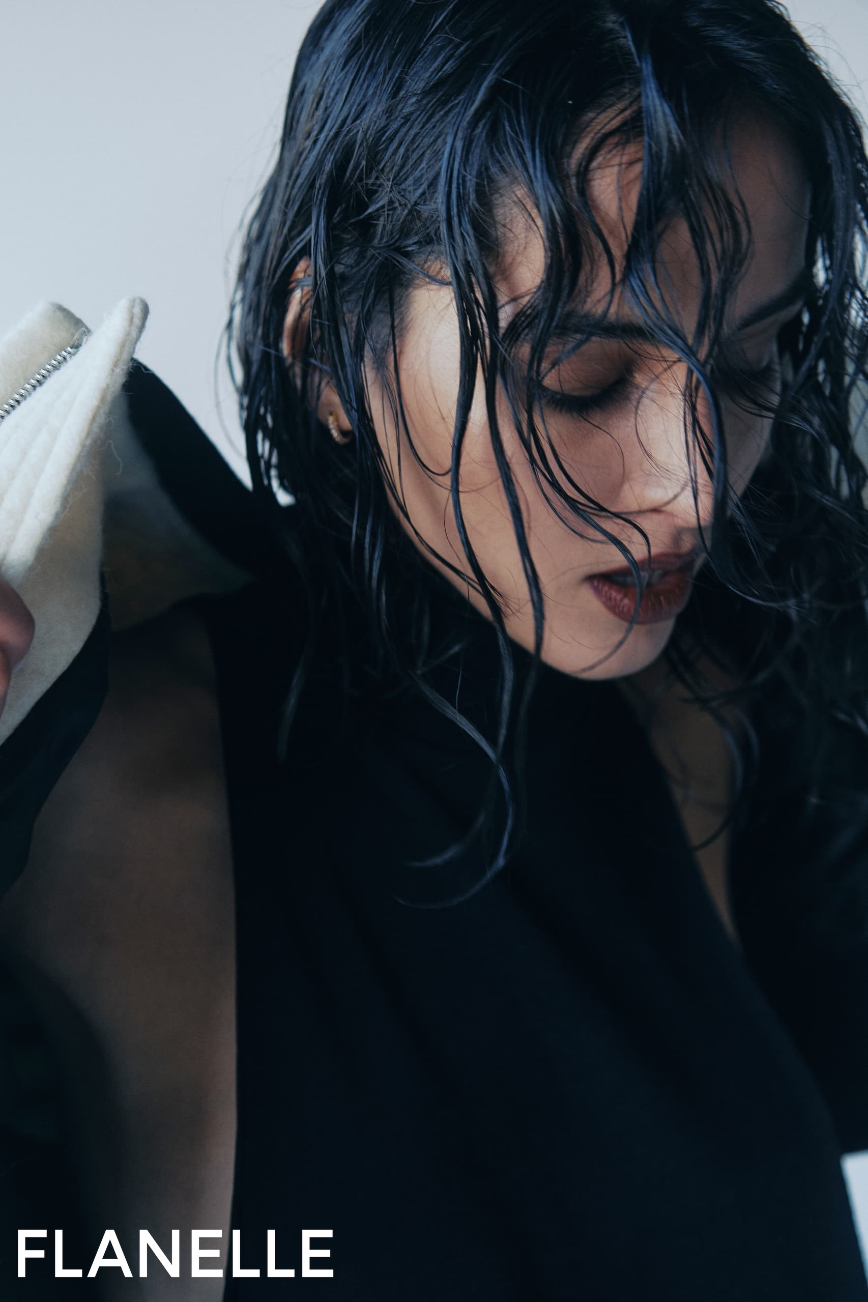 Model in black outfit with wet hair, posing for Flanelle fashion photoshoot.
