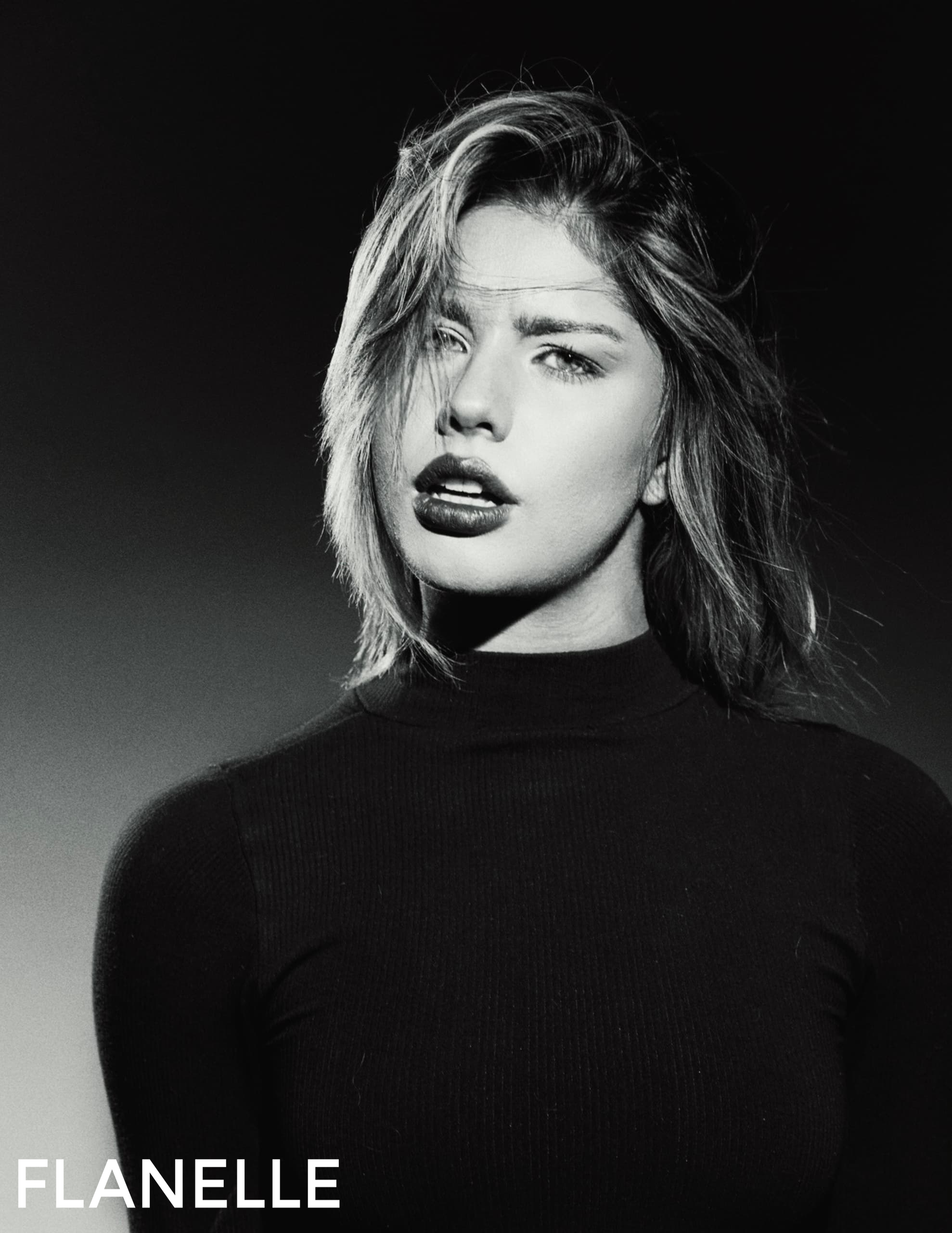 Black and white portrait of a woman with tousled hair, in a dark turtleneck.